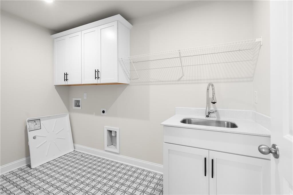 Modern laundry room featuring white shaker cabinets, deep utility sink, wire drying rack, and geometric tile floor in Davidson Homes The Hickory E, Buford, GA