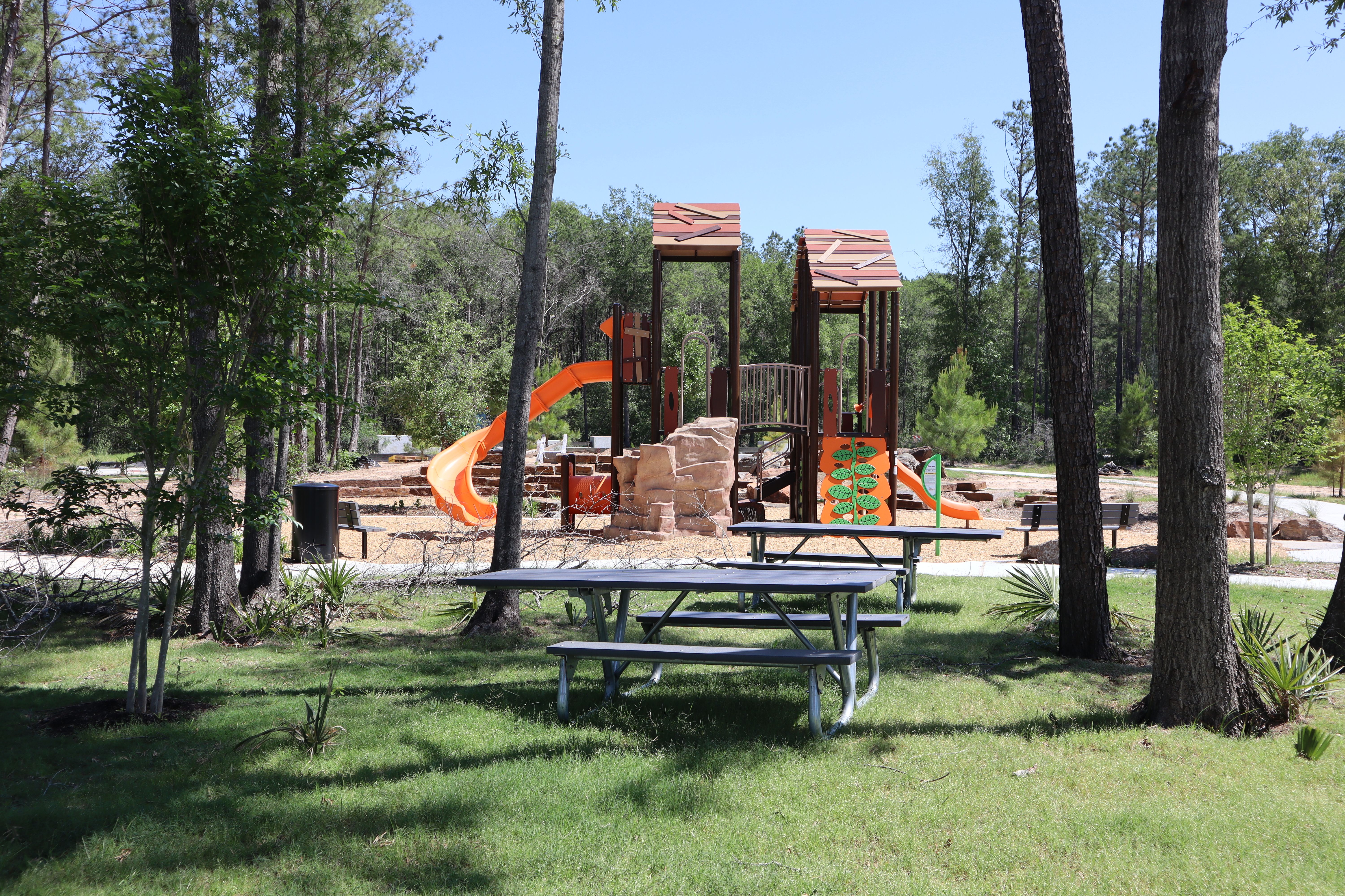 Children's playground at Robins Landing in Houston Texas featuring colorful slides, climbing towers, picnic table amid tall pines