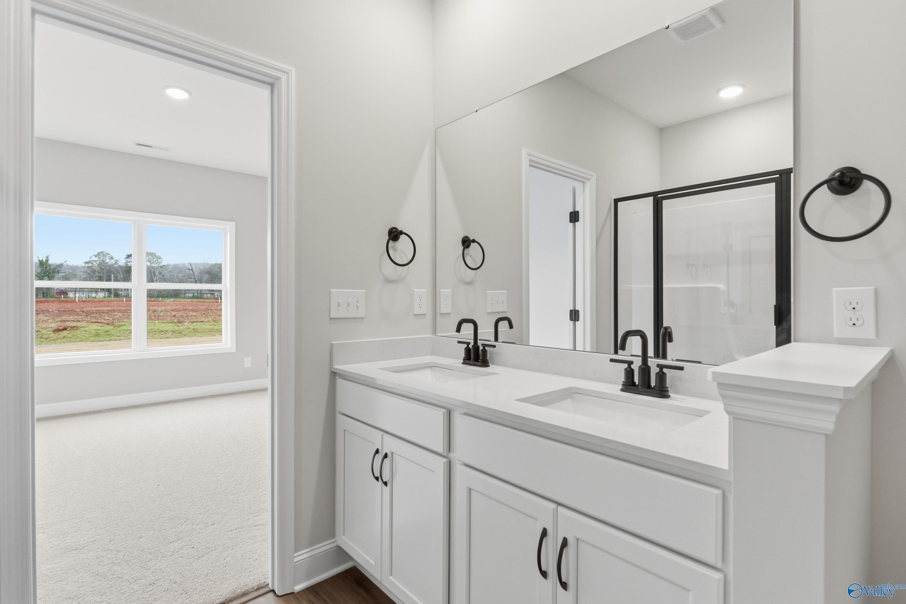 Modern master bathroom with double white vanity, black faucets, glass shower, and scenic window view in Davidson Homes The Asheville, Huntsville AL