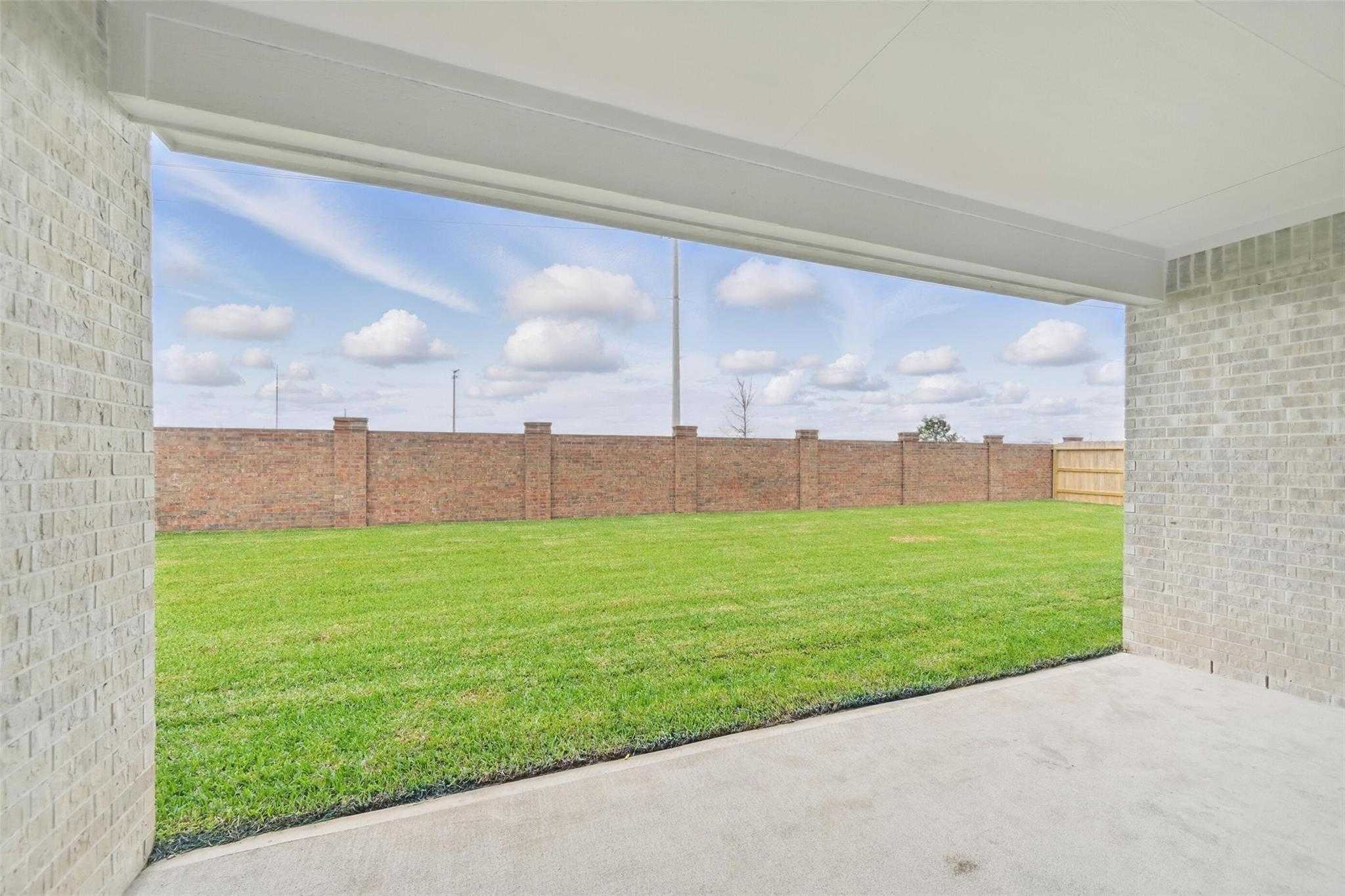 Covered back patio with lush green lawn and brick fence in Davidson Homes The Victoria C, Lago Mar, Texas City