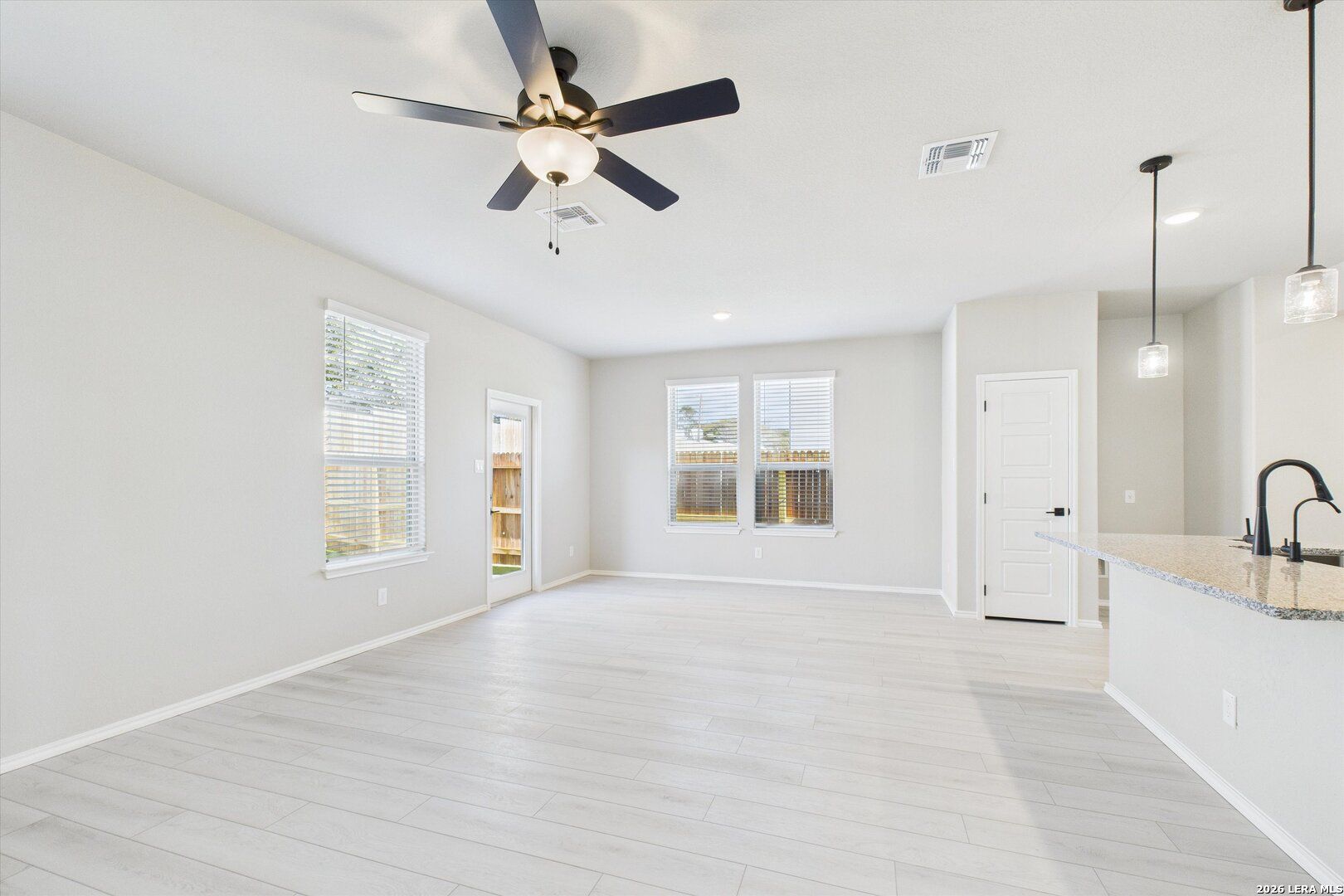 Open-concept living room and kitchen with light wood floors, ceiling fans, and pendant lights in Davidson Homes The Charlotte A, San Antonio