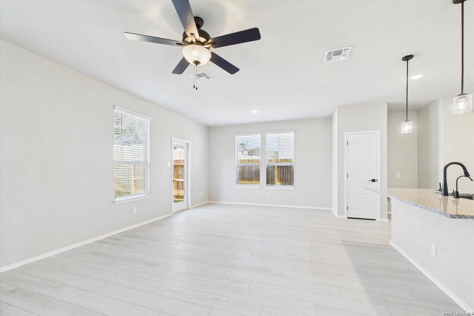 Open-concept living room and kitchen with light wood floors, ceiling fans, and pendant lights in Davidson Homes The Charlotte A, San Antonio