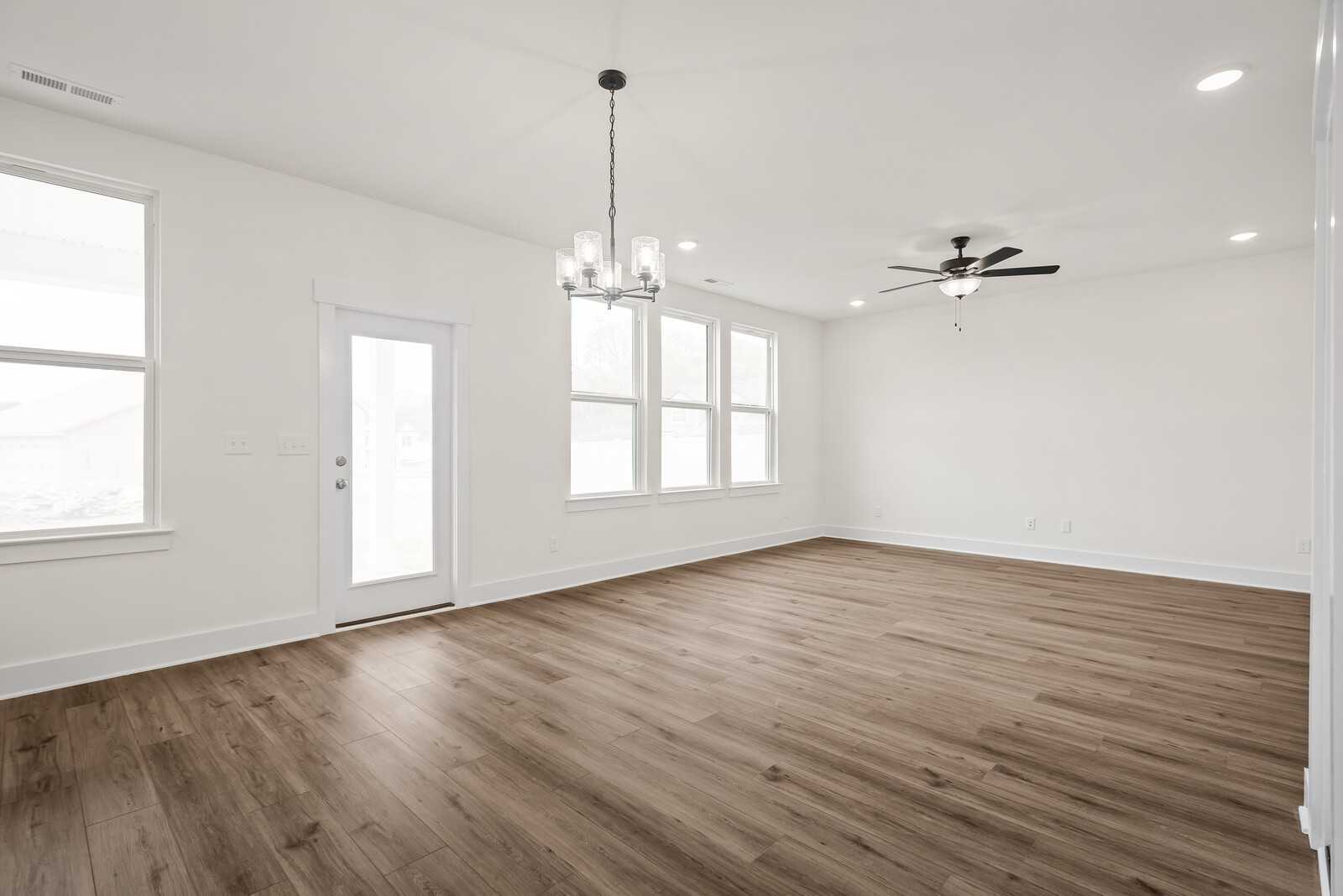 Spacious living room with hardwood floors, chandelier, ceiling fan, and large windows in The Logan C by Davidson Homes, Gallatin, TN