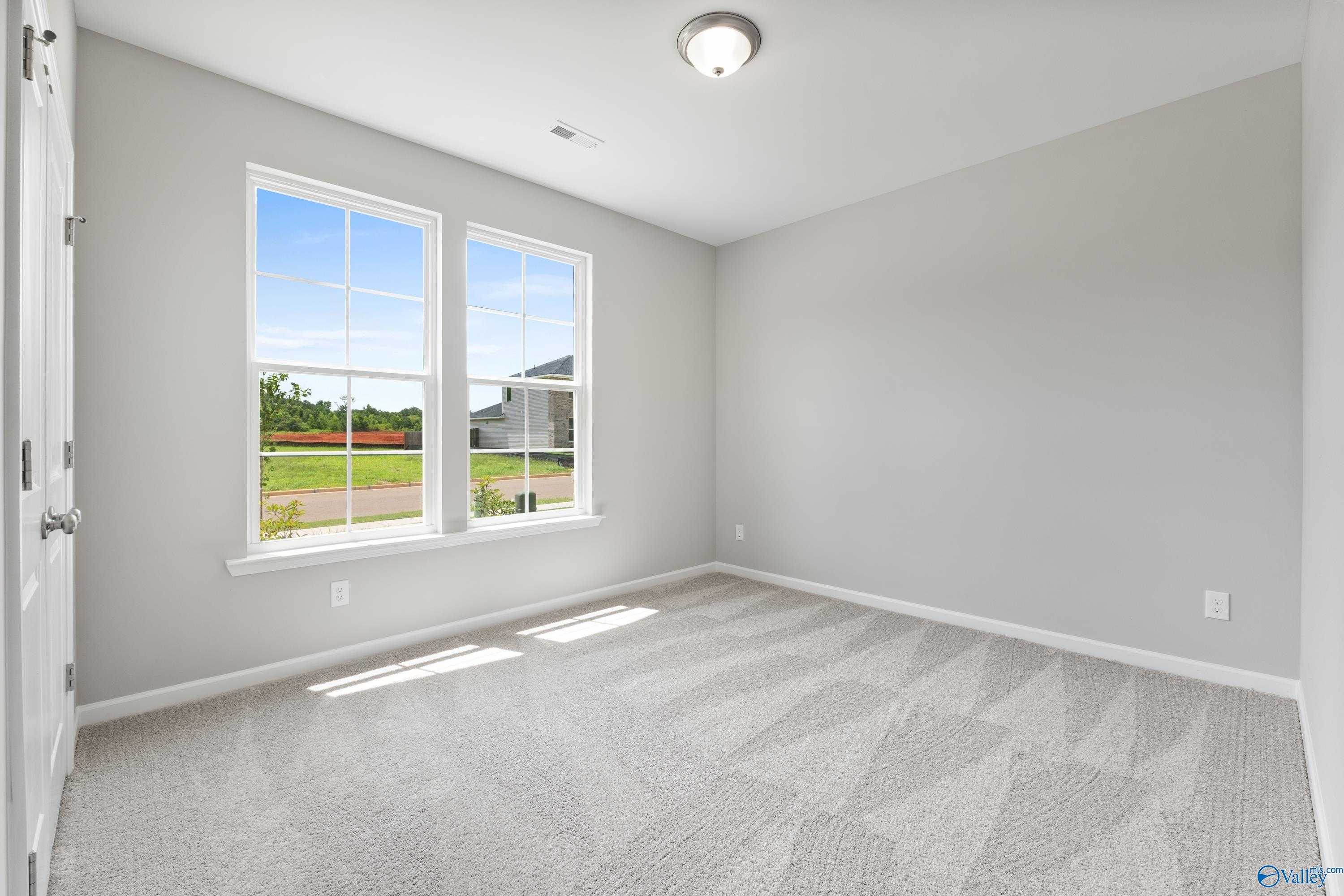 Bright secondary bedroom with gray walls, carpet flooring, and large windows overlooking green yard in Davidson Homes The Phoenix, Hazel Green, AL