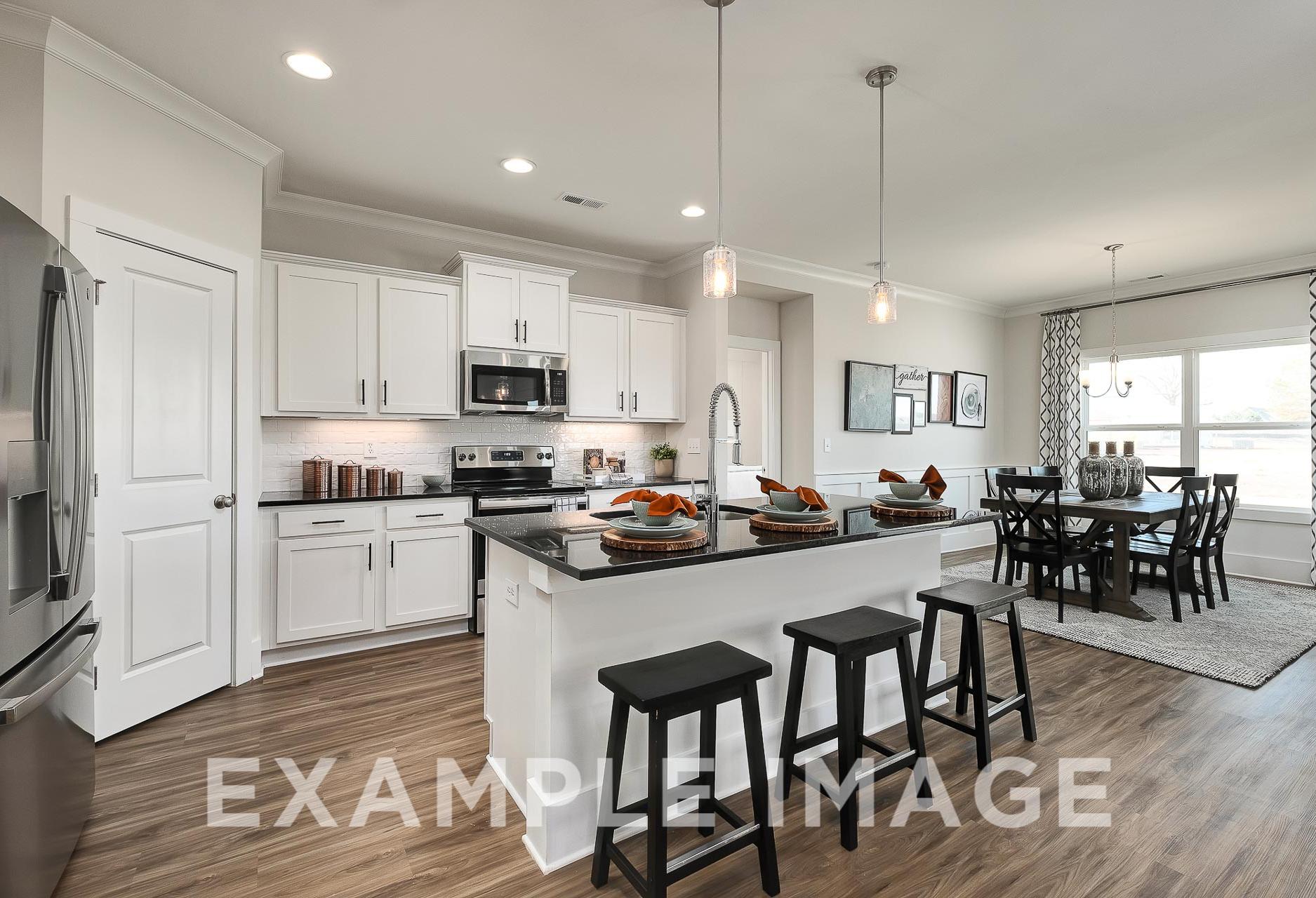 Modern open-concept kitchen in The Everett B featuring white cabinets, stainless appliances, granite island with bar stools, and dining area