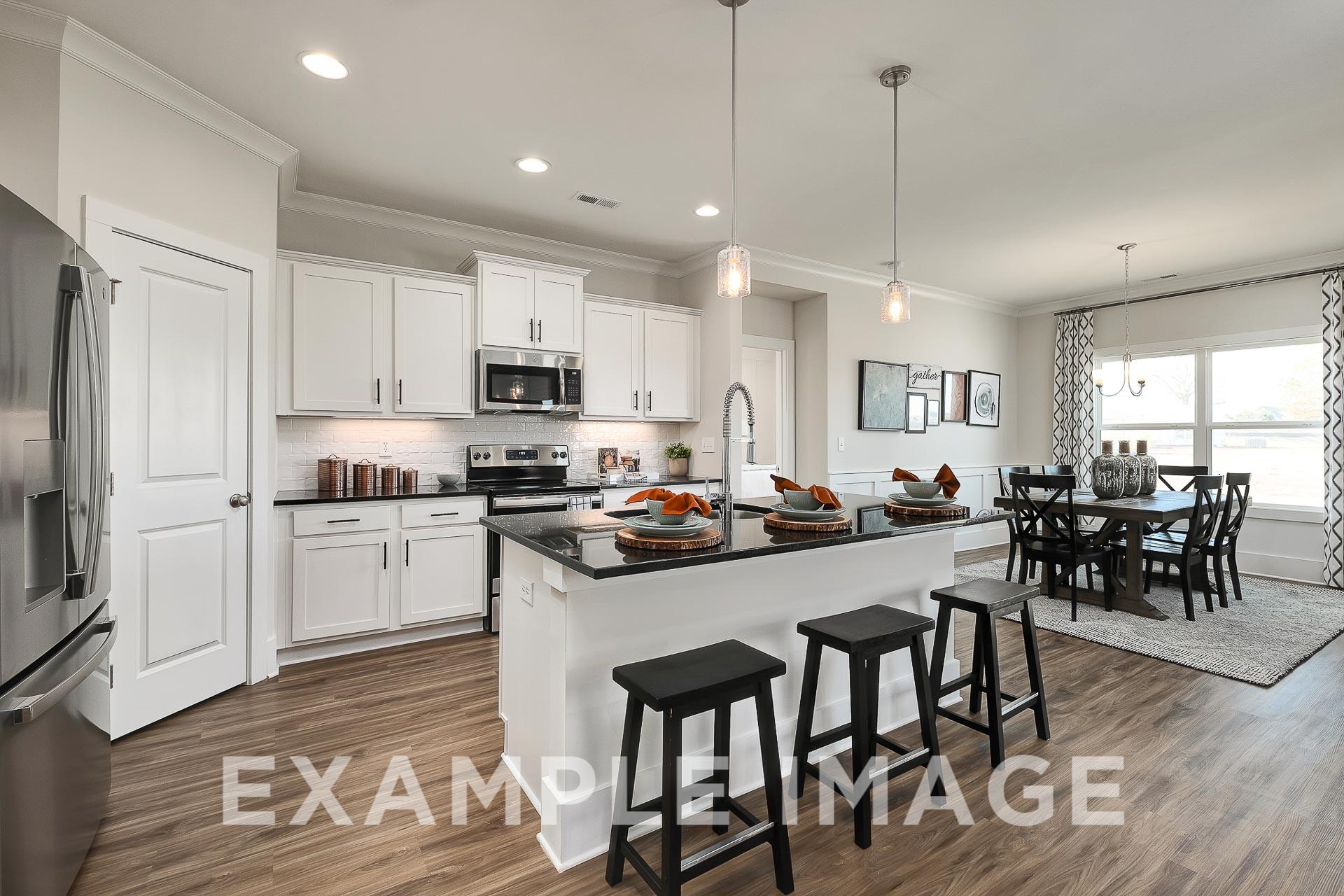 Modern open-concept kitchen in The Everett B featuring white cabinets, stainless appliances, granite island with bar stools, and dining area