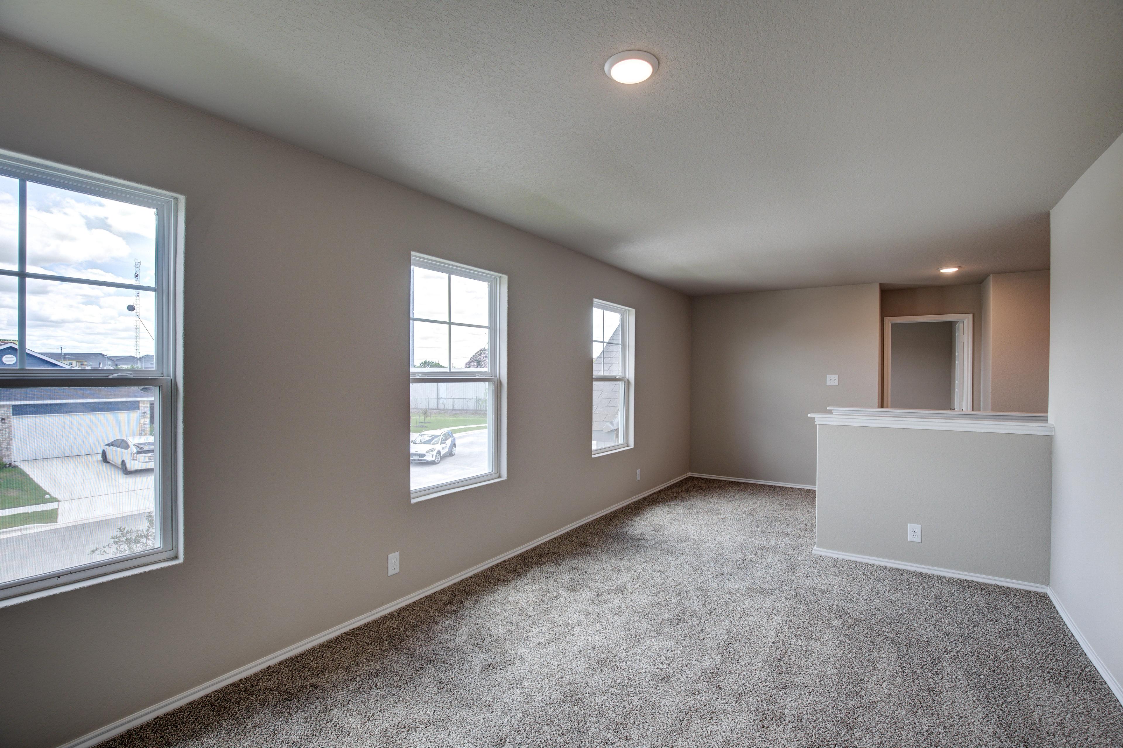 Spacious open living area in The Murray G with beige walls, large windows to suburban view, carpeted floor, and adjacent counter space