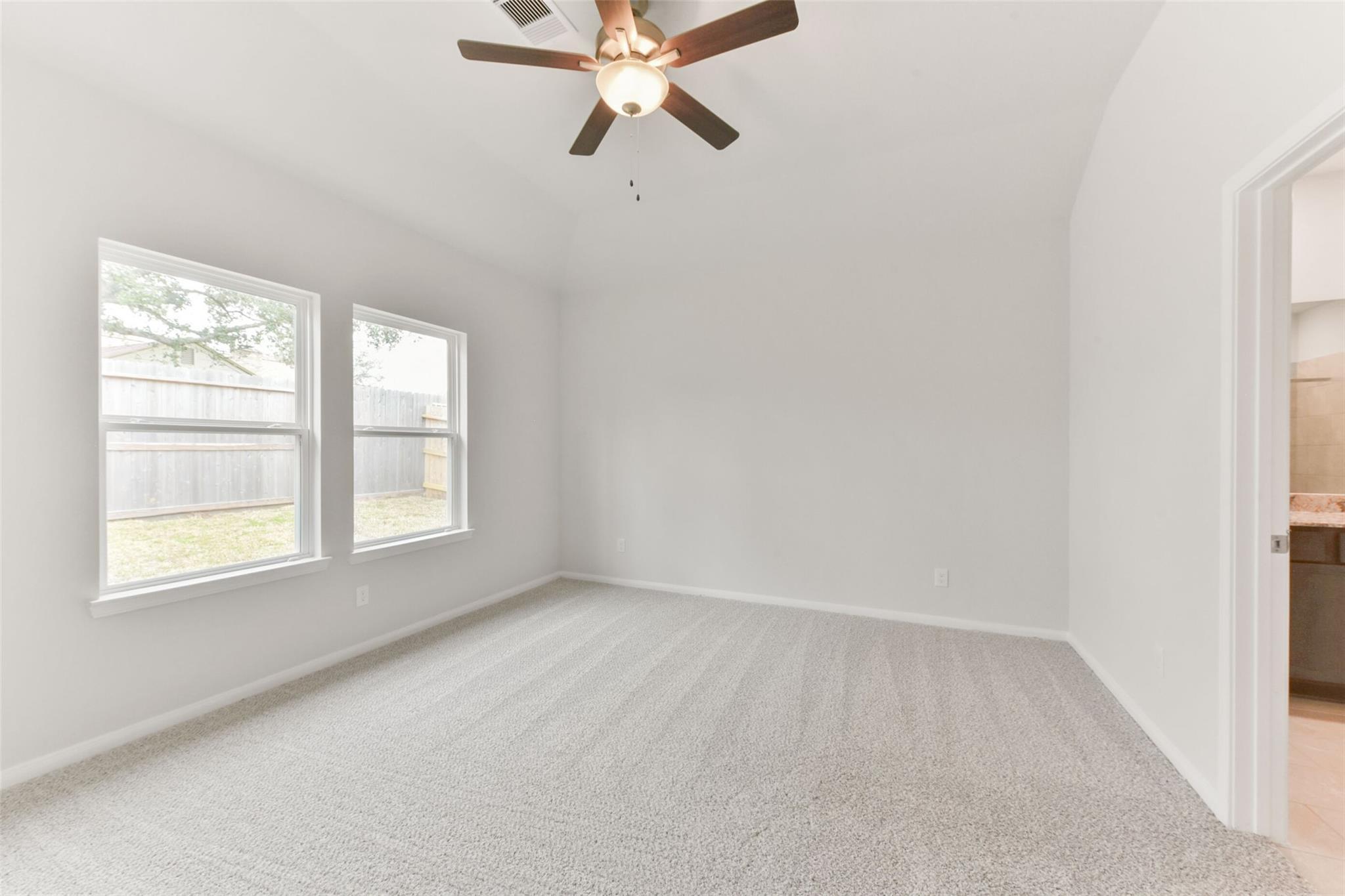 Bright secondary bedroom featuring ceiling fan, large windows, and plush carpet in Davidson Homes The Laguna B, Magnolia Texas