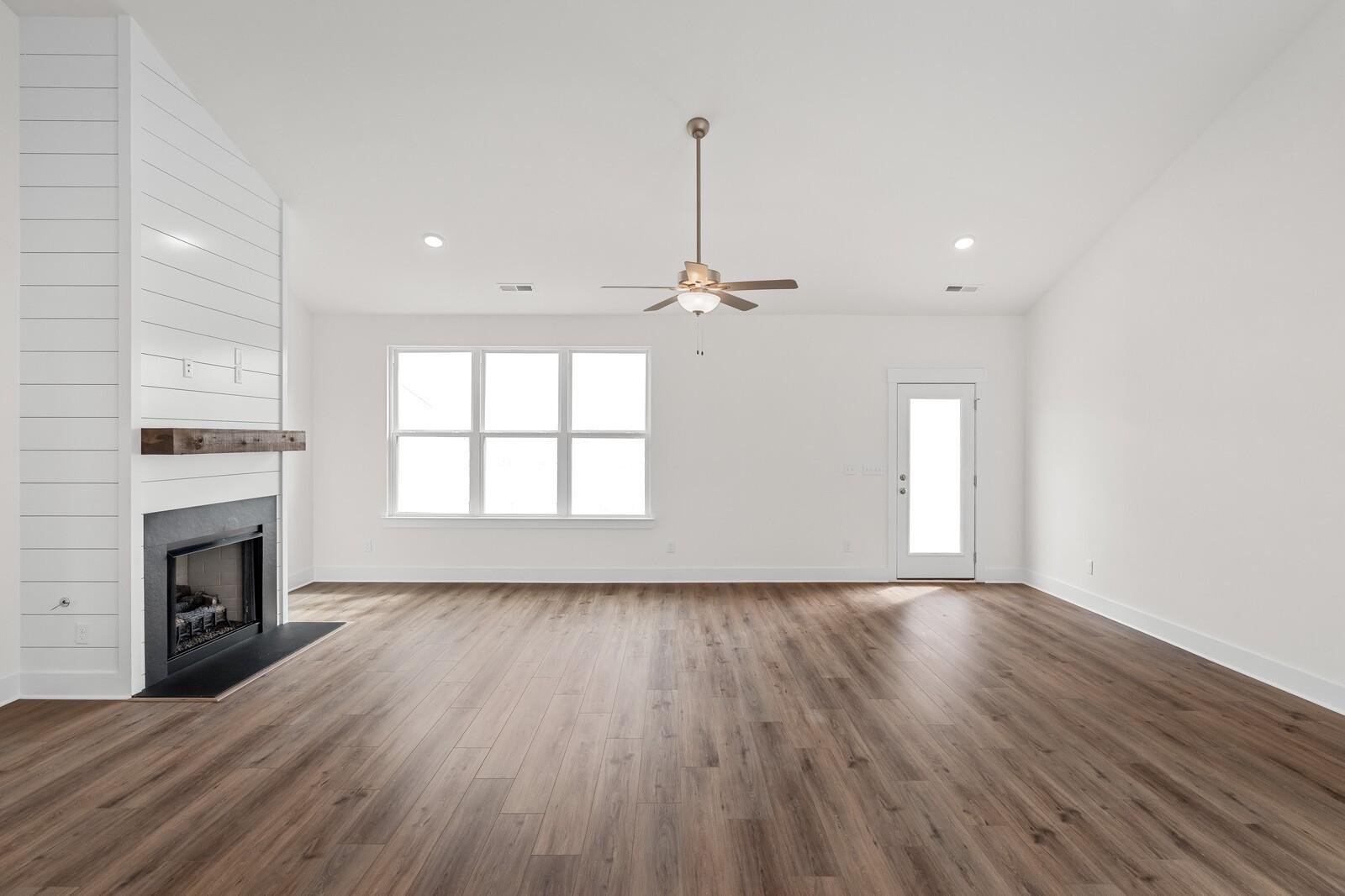 Spacious living room with shiplap fireplace wall, hardwood floors, large windows, and ceiling fan in Davidson Homes The Ridgeport, Gallatin, TN
