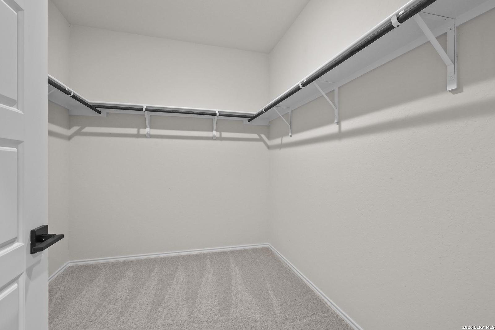 Spacious walk-in closet with dual hanging rods and carpet flooring in The Glenwood E floor plan at Comanche Ridge, San Antonio