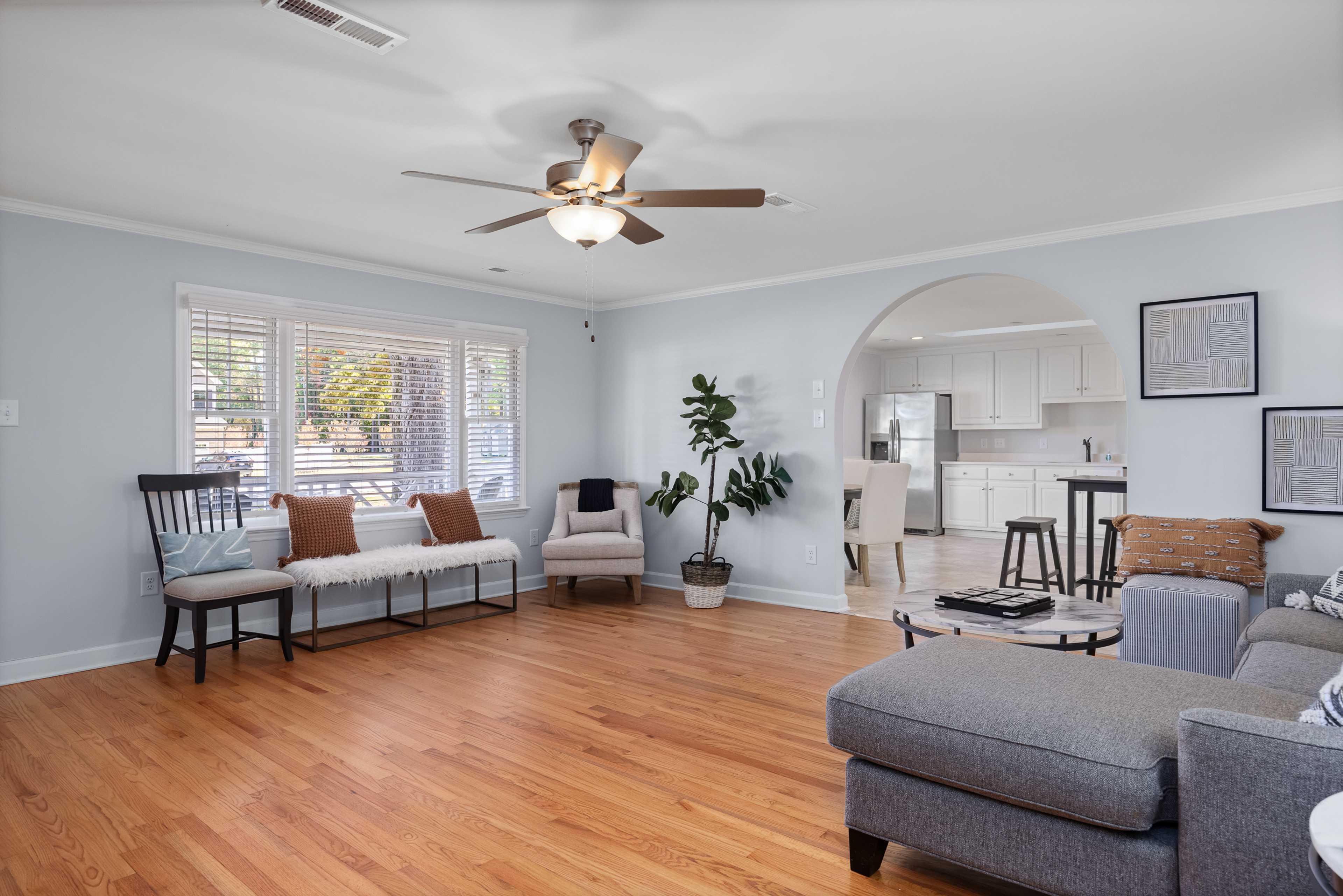 Open-concept living room at Stagecoach Corner in Mebane NC with hardwood floors, ceiling fan, and archway to white kitchen