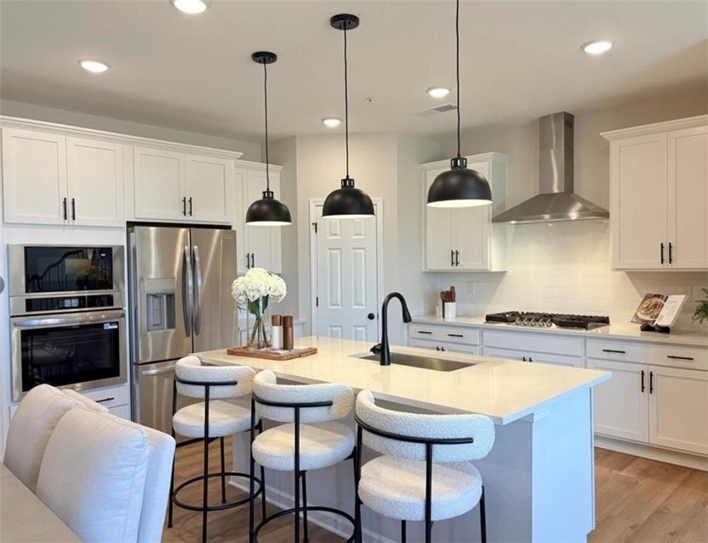 Modern white kitchen with quartz island, bar stools, stainless appliances, and pendant lights in Davidson Homes The Durham D, Cumming GA