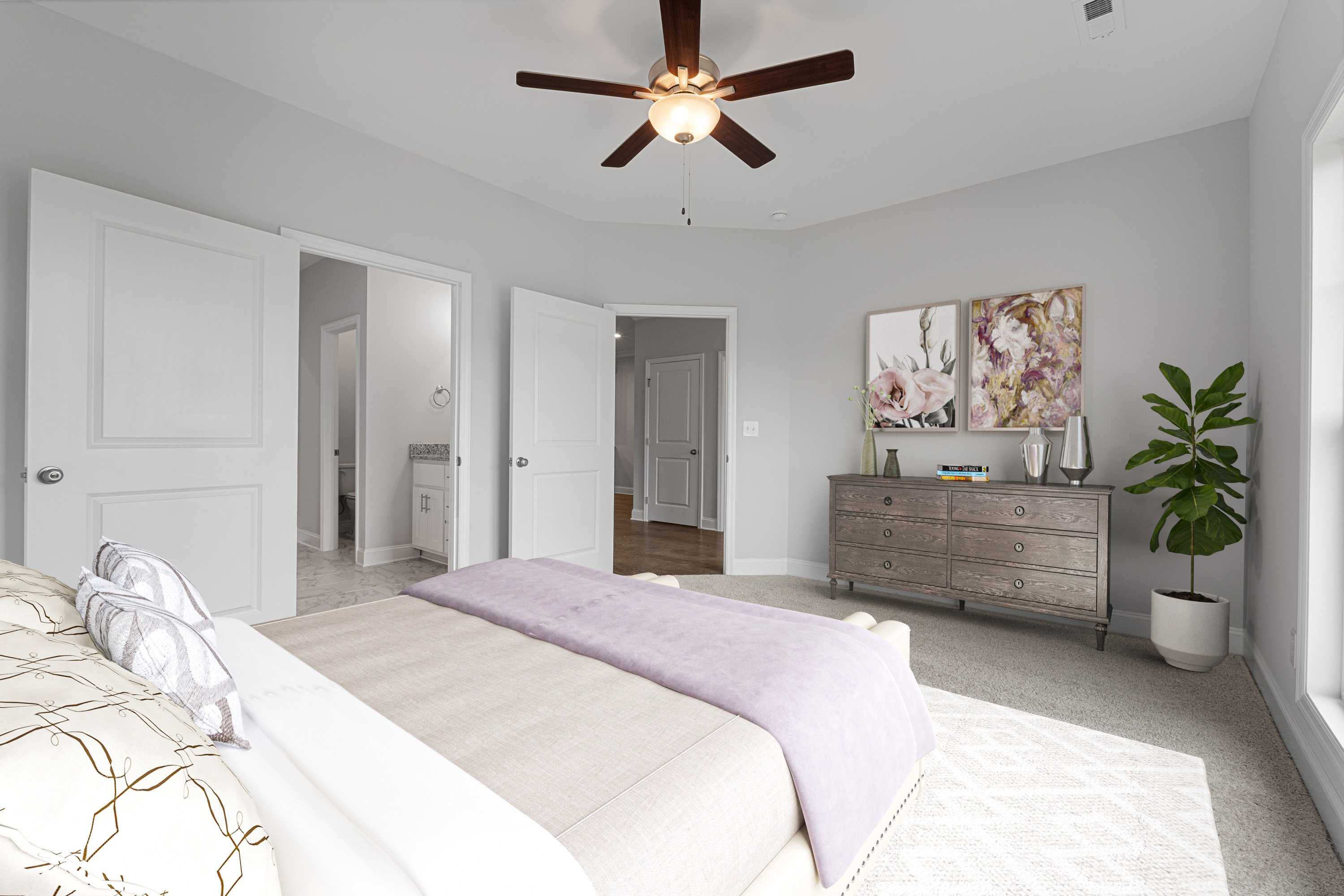 Spacious primary bedroom at The Villas at Barnett's Crossing in Madison, Alabama with ceiling fan, king bed, dresser and en-suite bath