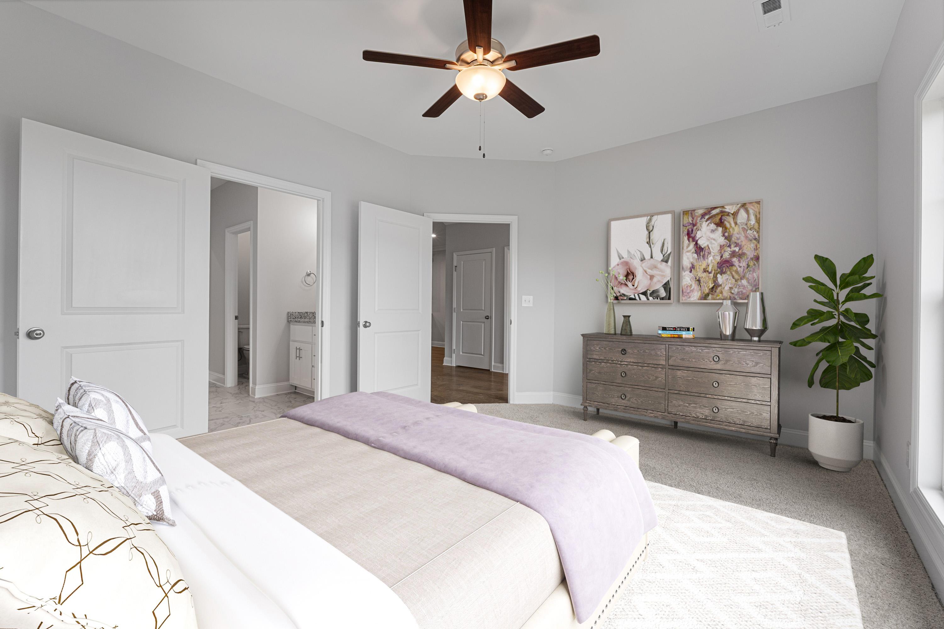 Spacious primary bedroom at The Villas at Barnett's Crossing in Madison, Alabama with ceiling fan, king bed, dresser and en-suite bath