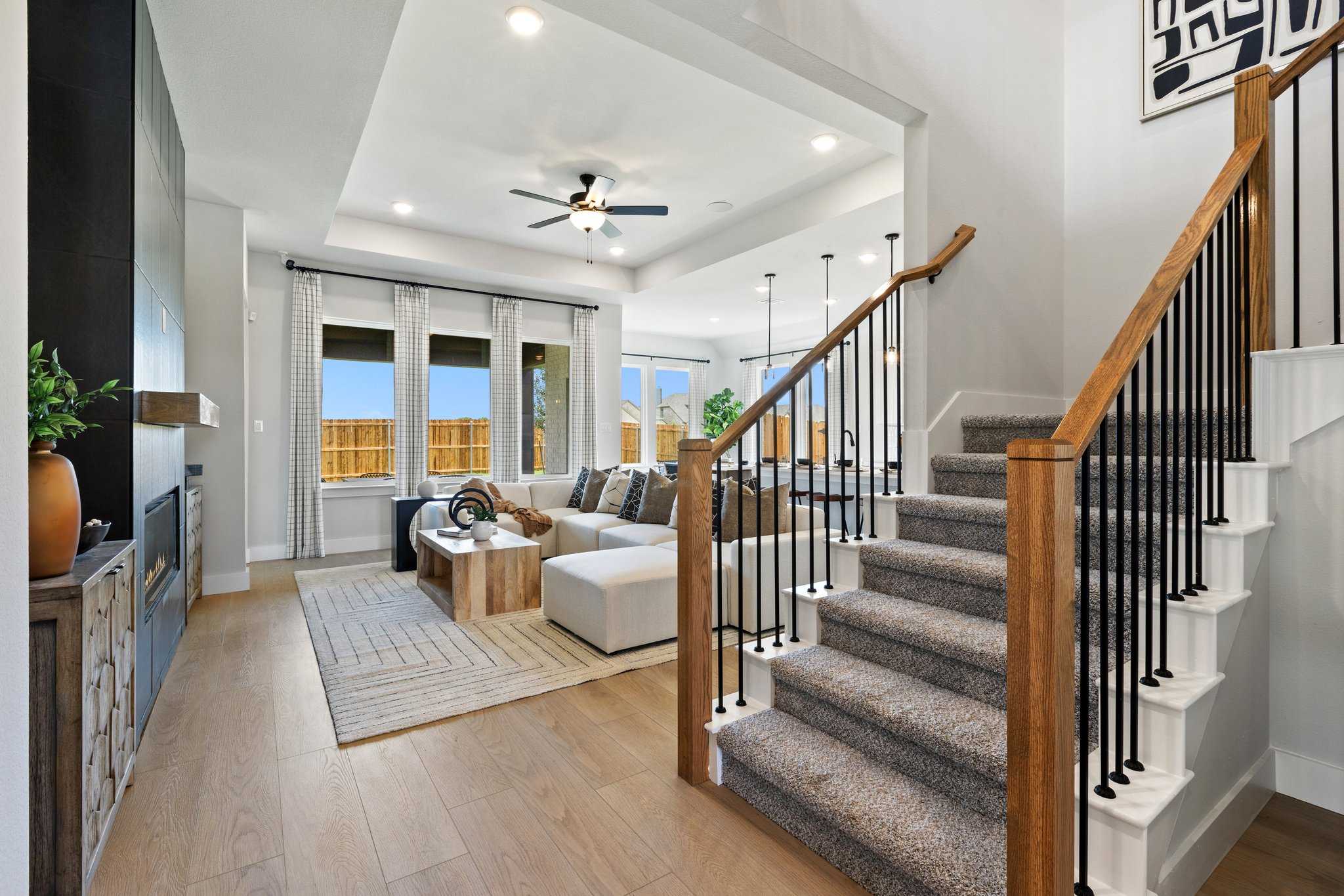 Spacious open living room with fireplace, white sofa, plants, and grand wooden staircase in Davidson Homes The Sequoia N, Josephine, Texas
