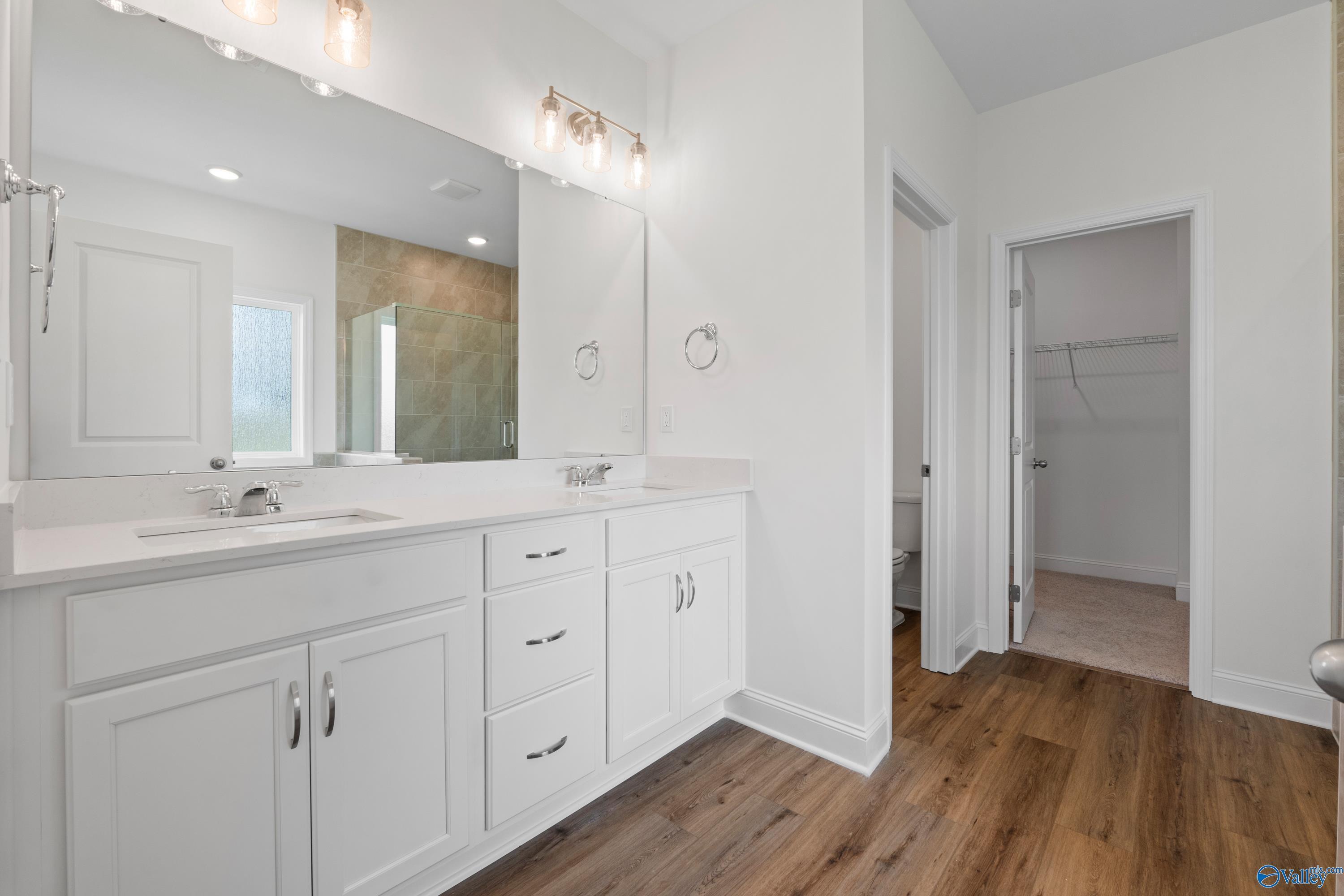 Modern primary bathroom with double vanity, white cabinets, and walk-in closet in The Everett B, The Meadows, Athens, AL.