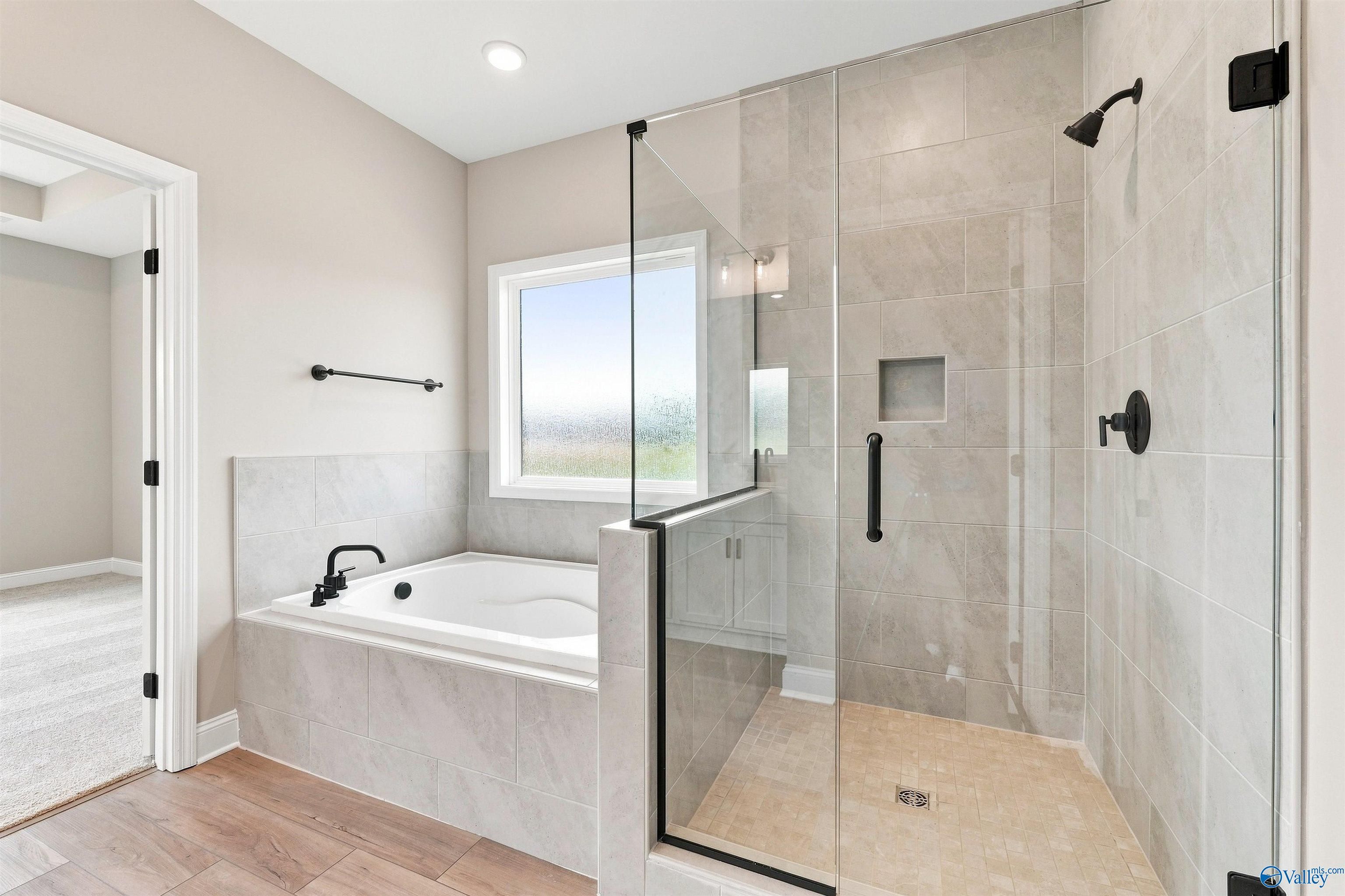 Modern primary bathroom with a tiled soaking tub and glass-enclosed shower in The Montgomery floor plan at Kendall Downs.