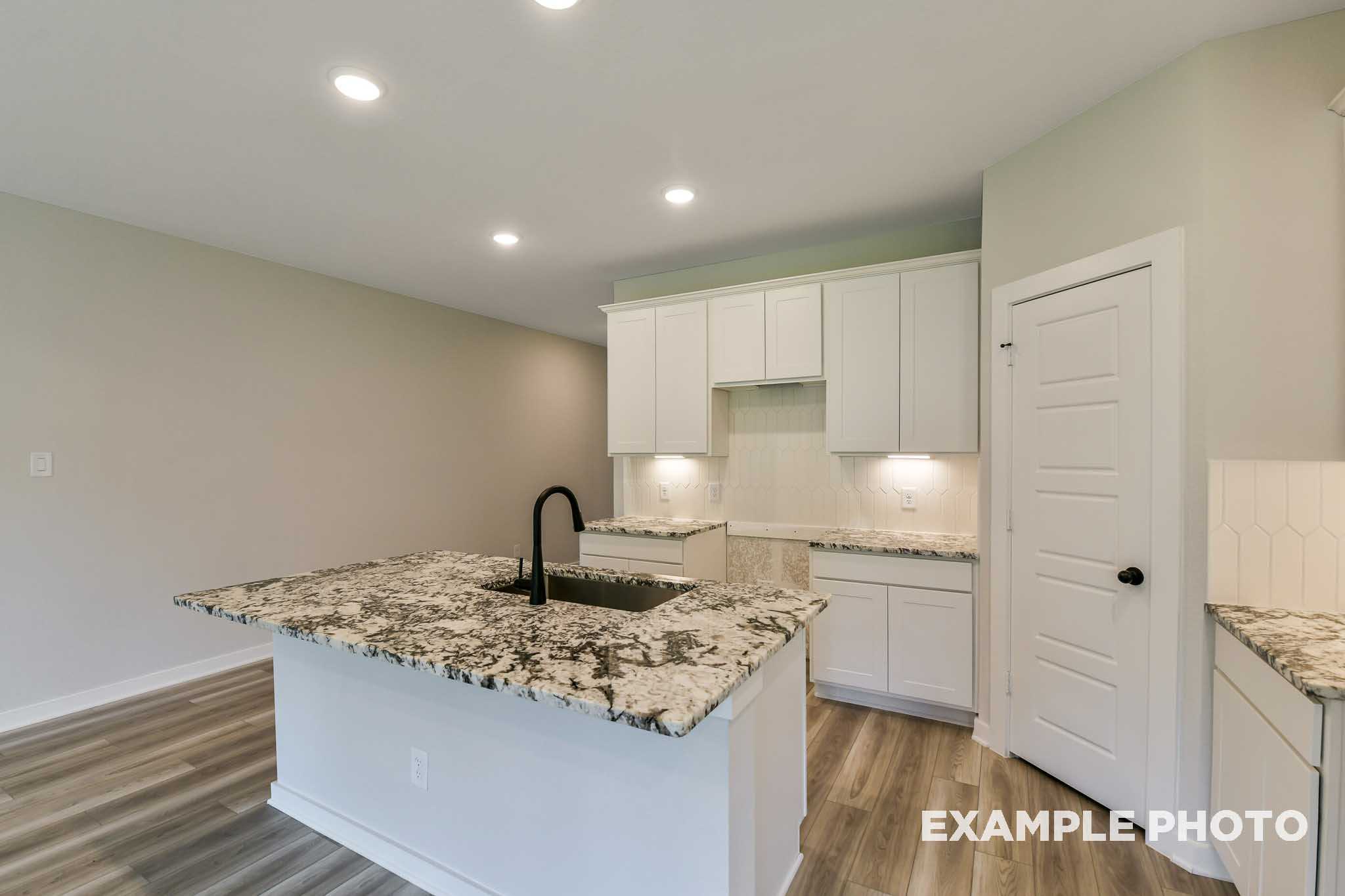 Spacious kitchen in The Daphne G home featuring white shaker cabinets, speckled granite island, black faucet, hardwood floors