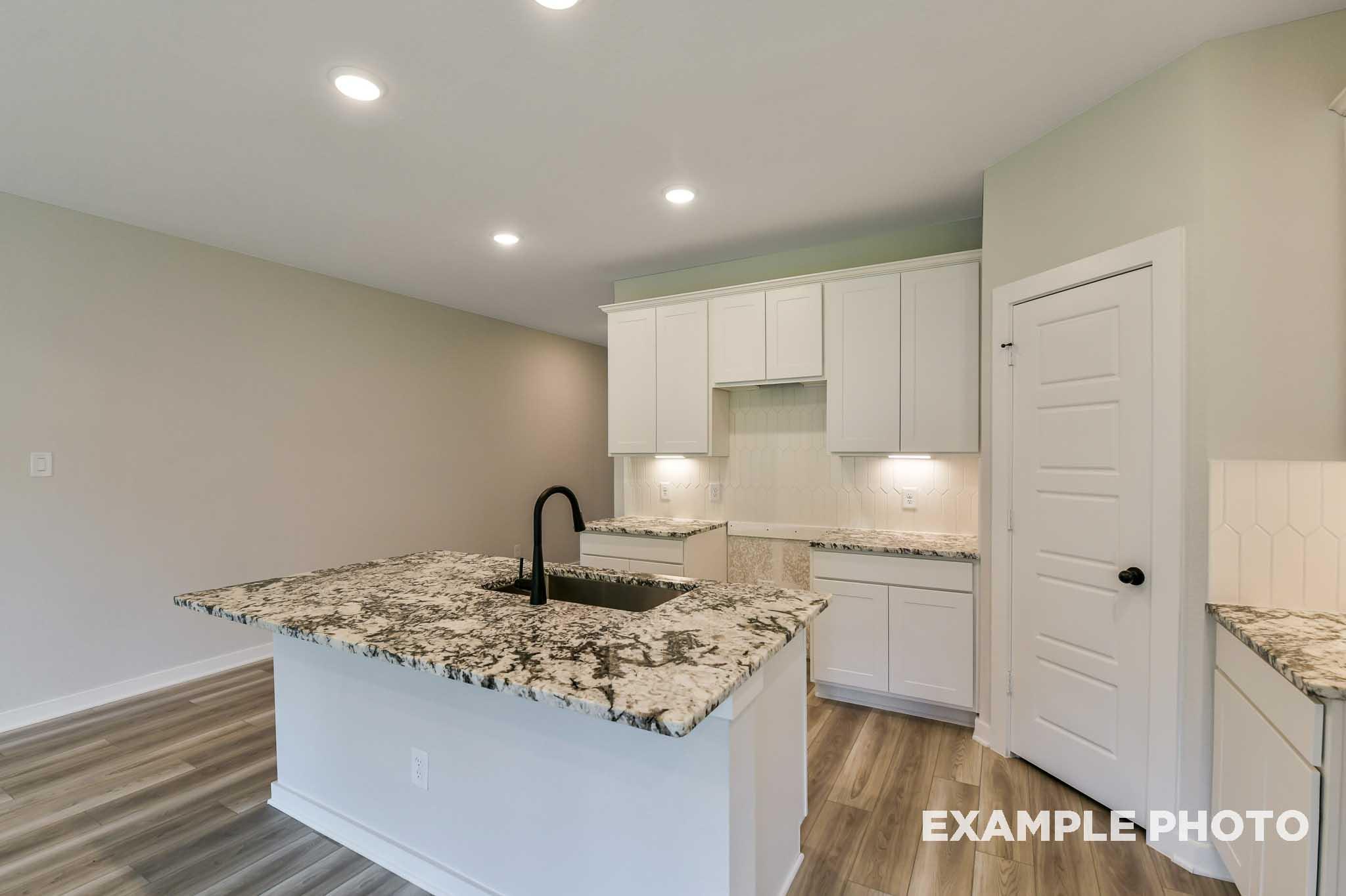 Spacious kitchen in The Daphne G home featuring white shaker cabinets, speckled granite island, black faucet, hardwood floors