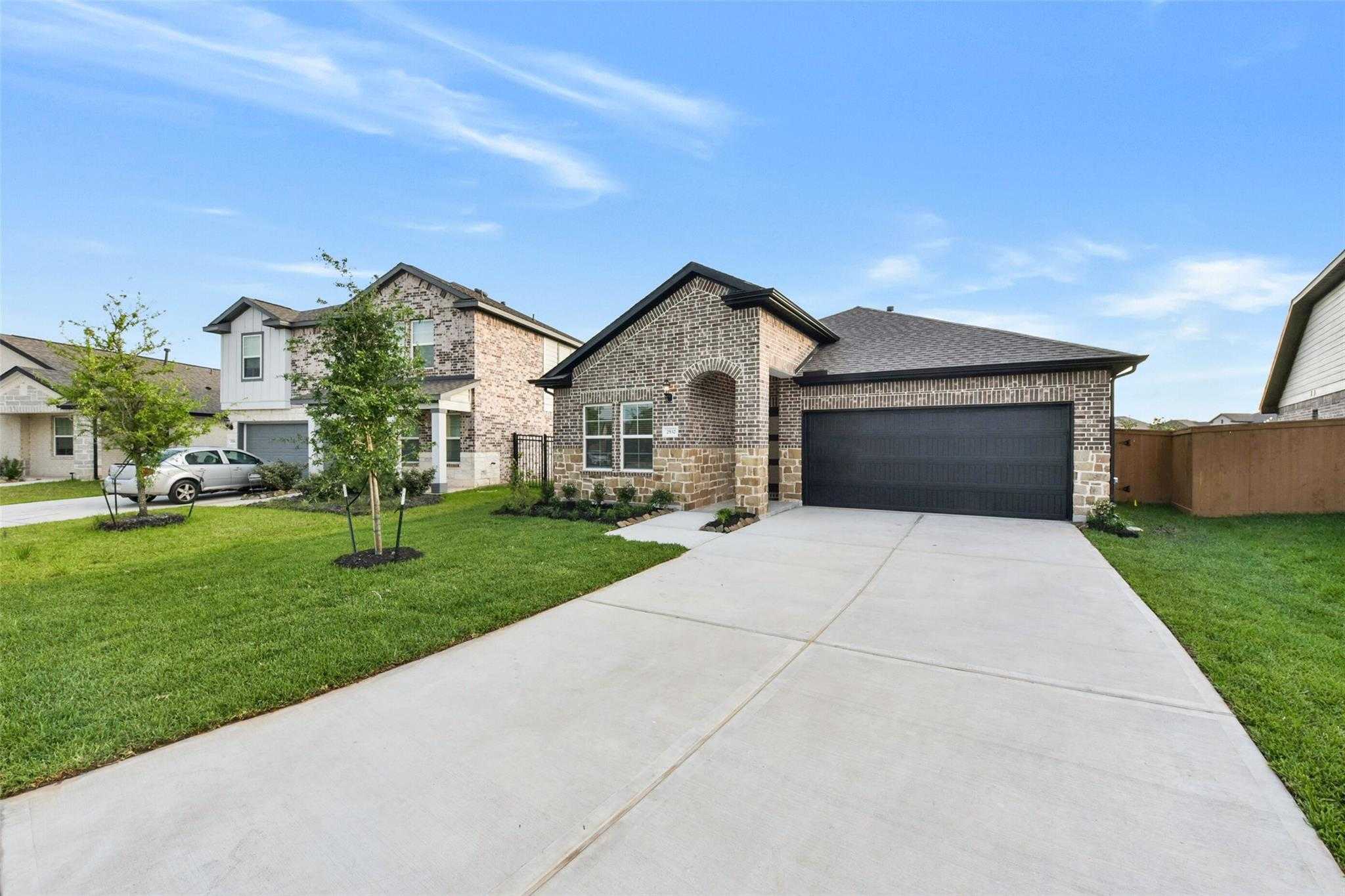 Modern 1-story brick home with 2-car garage, driveway, and lush green lawn in Sunterra, Katy, Texas