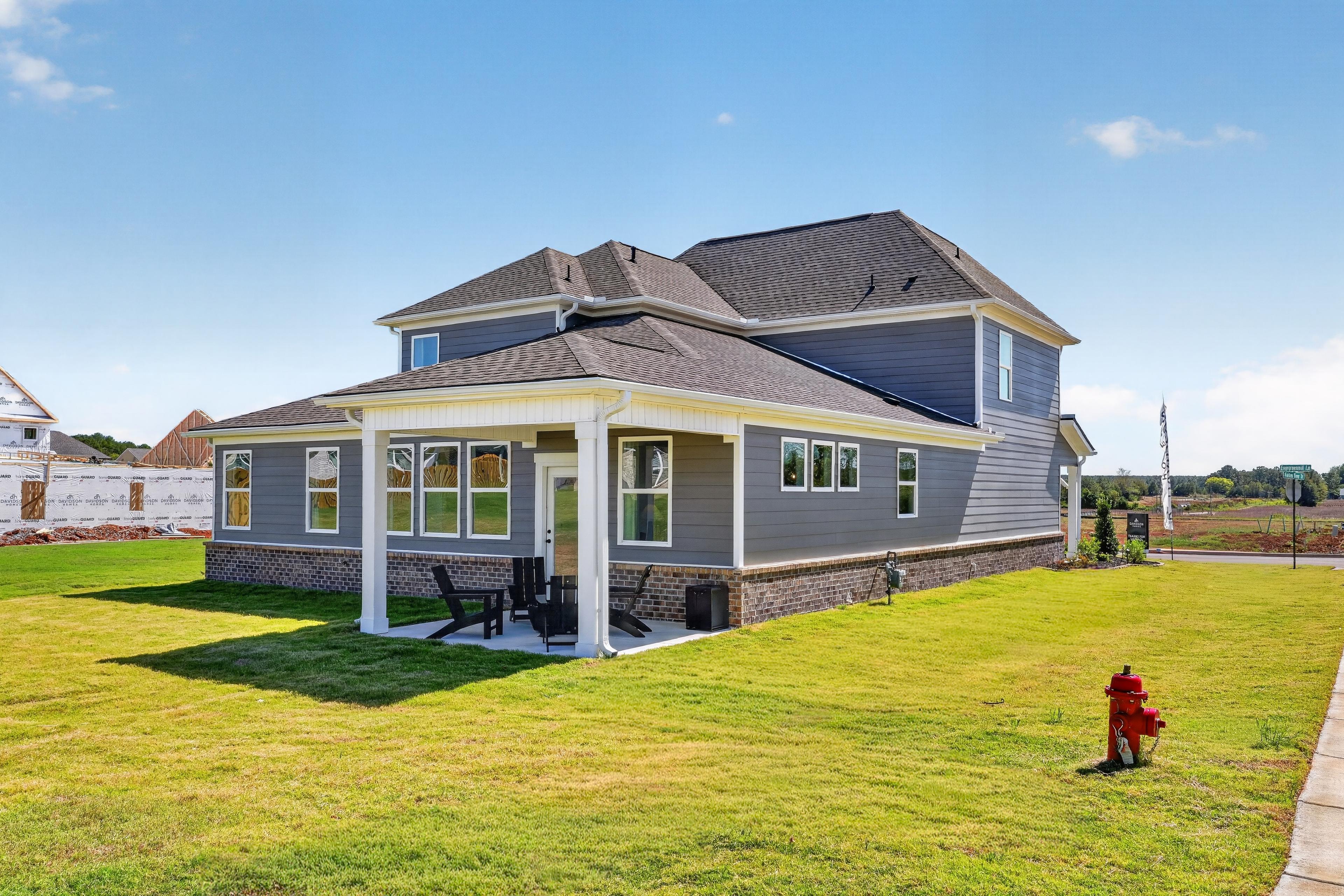 Gray two-story home with covered porch and Adirondack chairs at Evergreen Mill by Davidson Homes in Madison, Alabama