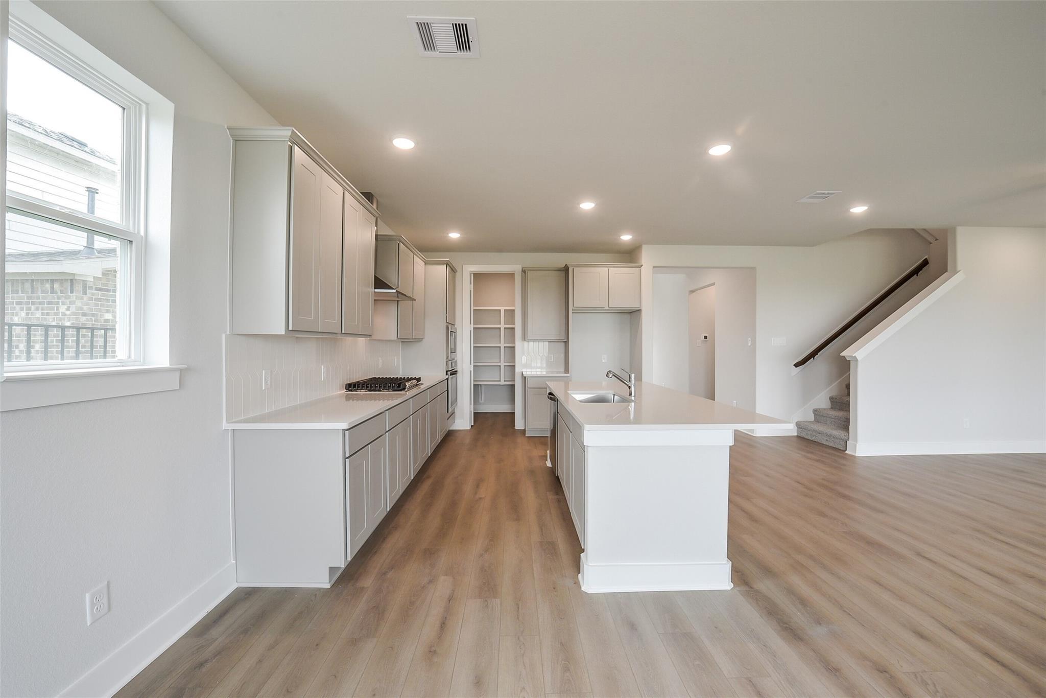 Modern open-concept kitchen with white cabinets, large island sink, and hardwood floors in Davidson Homes Philip B, Rosharon Texas