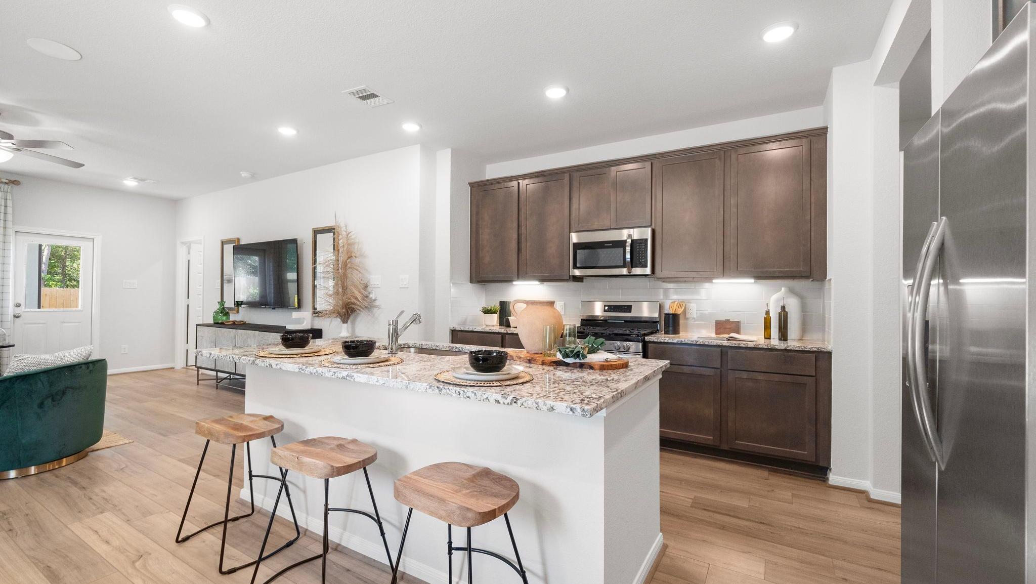 Modern kitchen with granite island, bar stools, and dark wood cabinets in a new Davidson Homes model at Robins Landing.