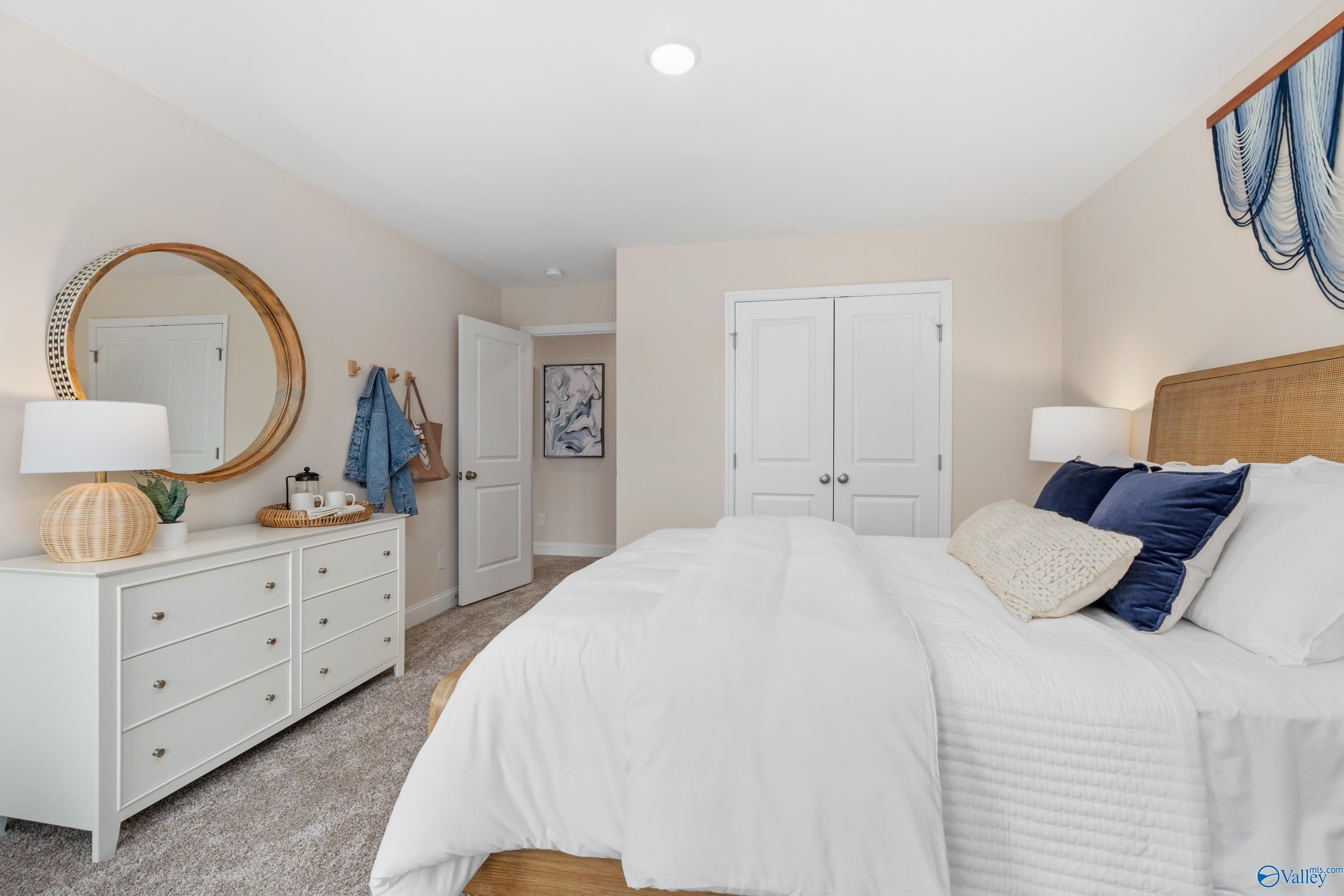 Serene master bedroom with rattan headboard, white duvet, blue pillows, gold mirror, and closet doors in Davidson Homes The Camden, Huntsville