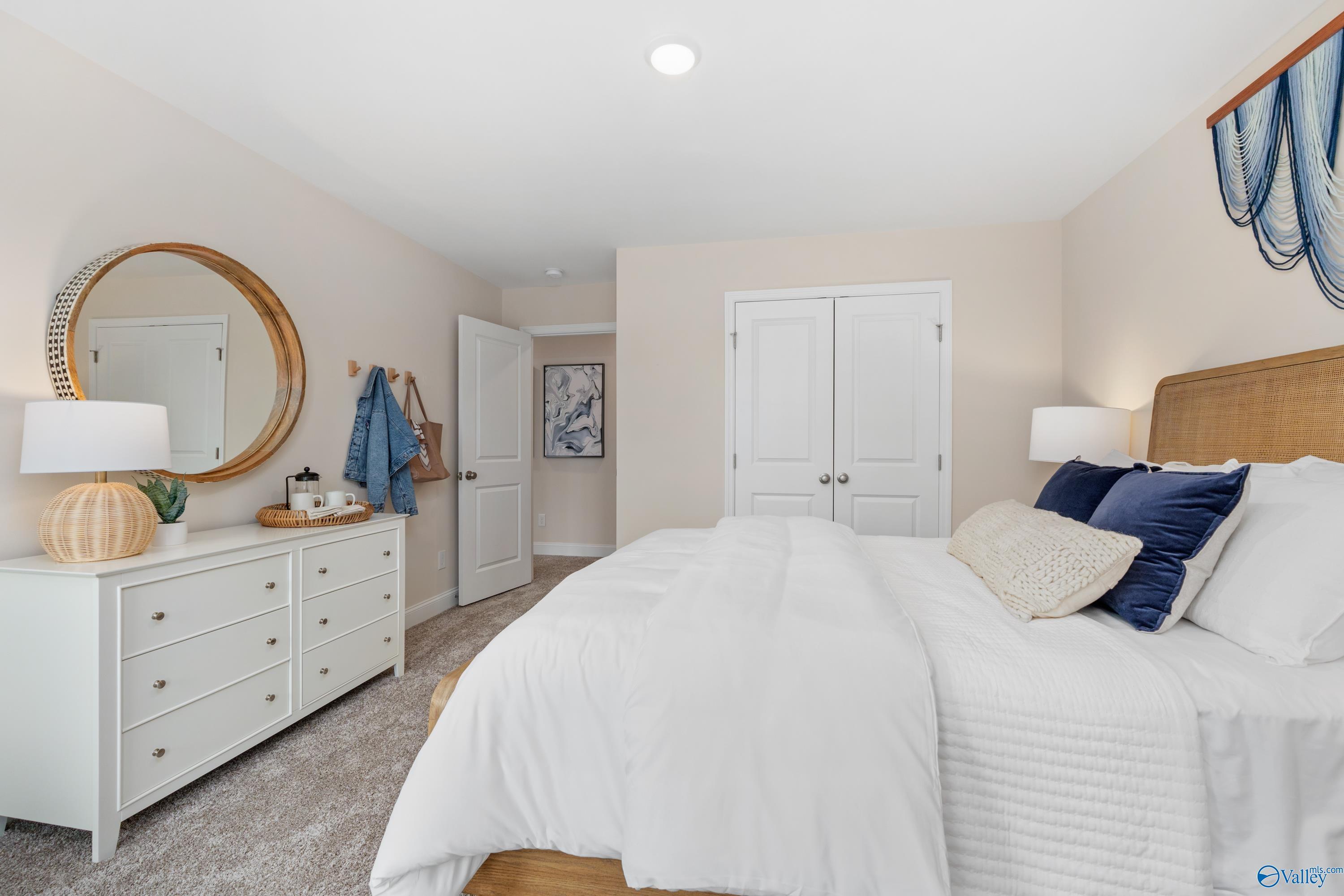 Serene master bedroom with rattan headboard, white duvet, blue pillows, gold mirror, and closet doors in Davidson Homes The Camden, Huntsville