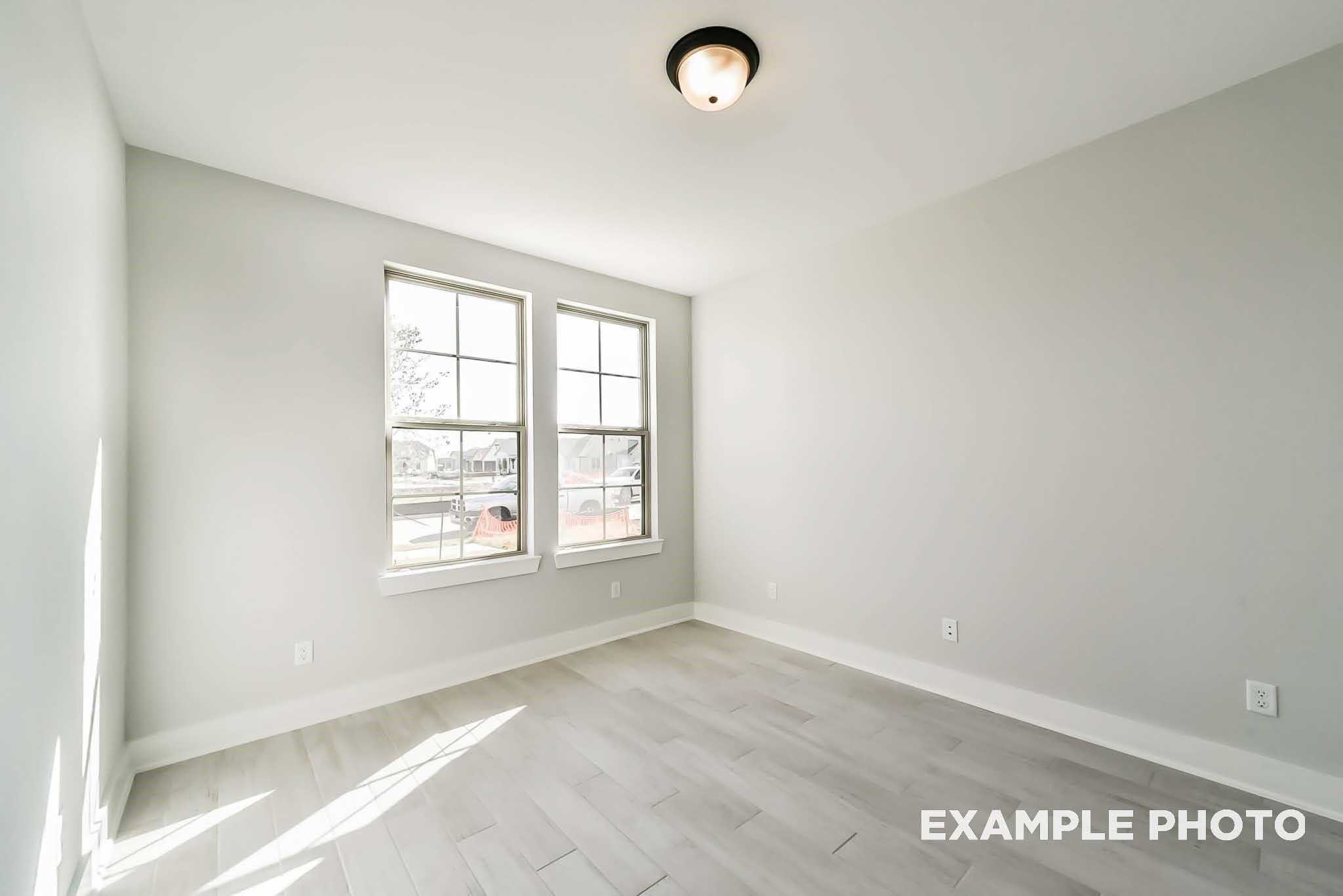 Bright bedroom with gray walls, large windows, and light wood floors in Davidson Homes The Philip C, Rosharon, Texas