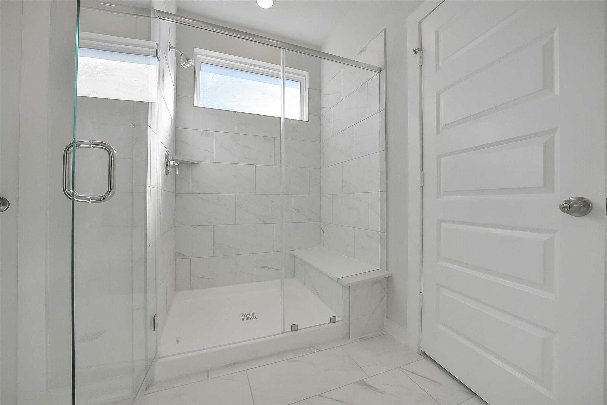 Modern walk-in shower with white subway tiles, glass enclosure, and bench in master bath, Davidson Homes The Acadia A, Sunterra Katy Texas