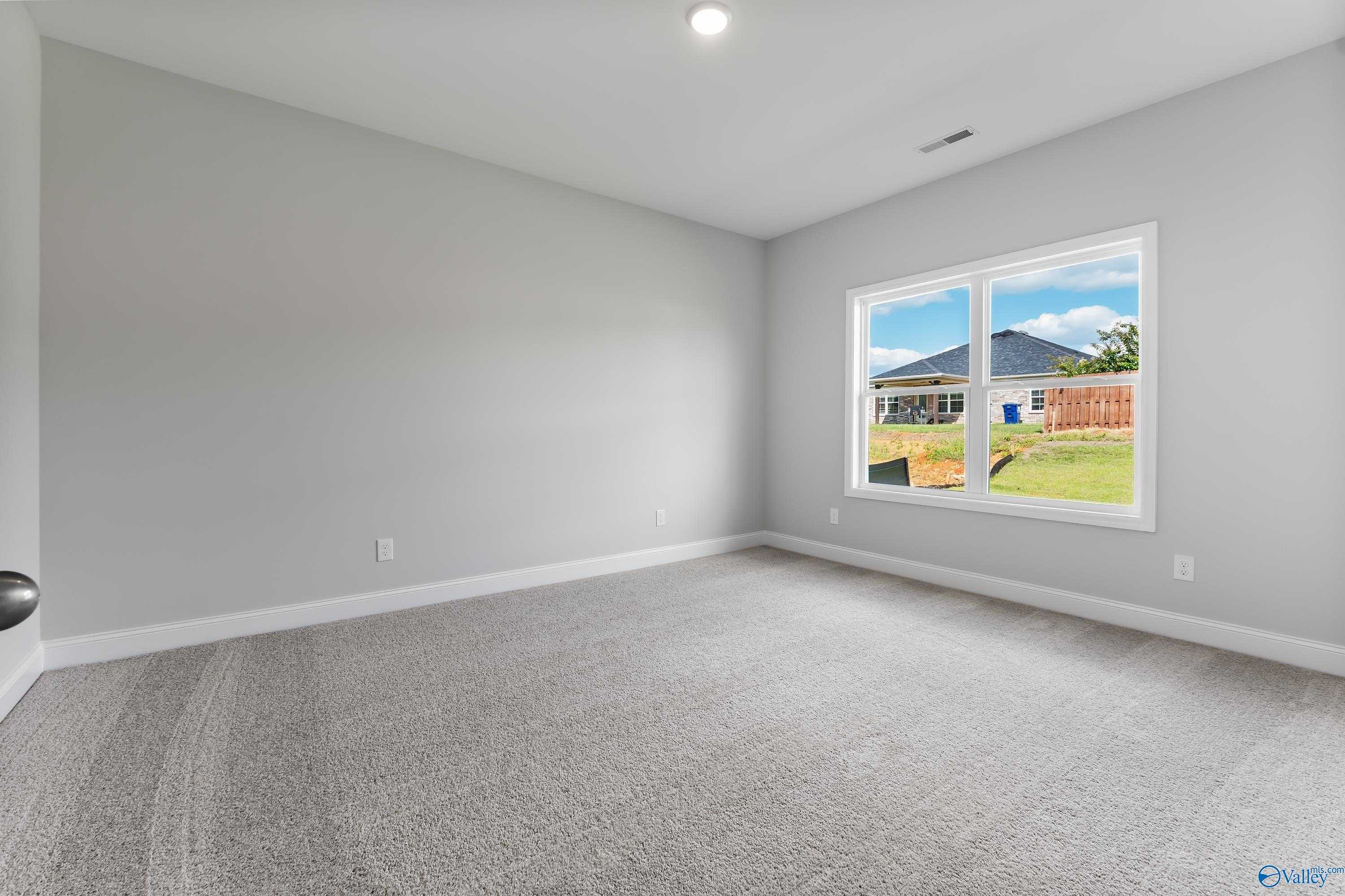 Bright secondary bedroom with neutral gray walls, carpet flooring, and large window view of backyard in Davidson Homes The Franklin C, Toney, Alabama