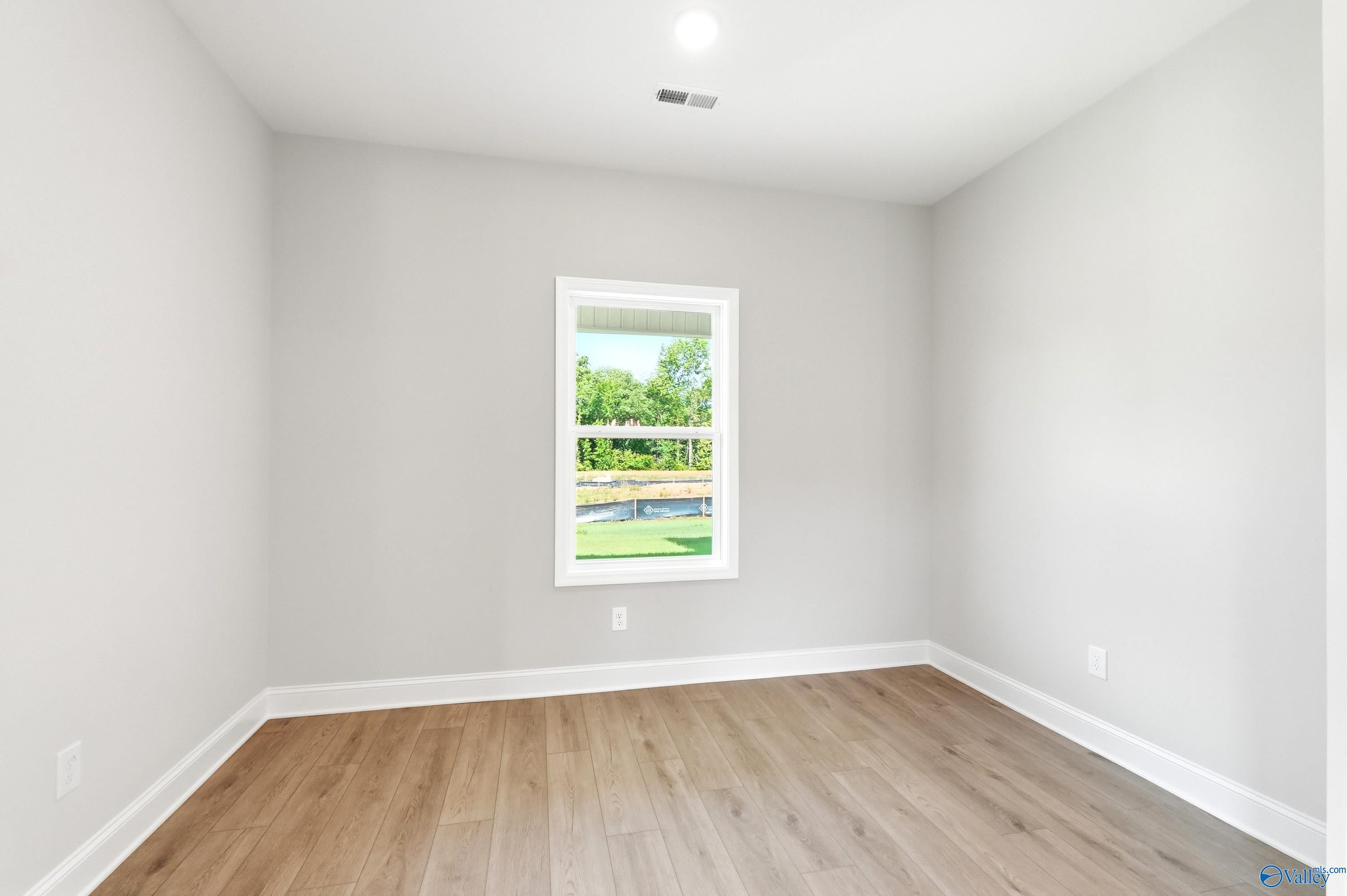 Spacious bedroom with neutral walls and wood-look flooring in The Russell A floor plan at Spragins Cove, Huntsville, AL.
