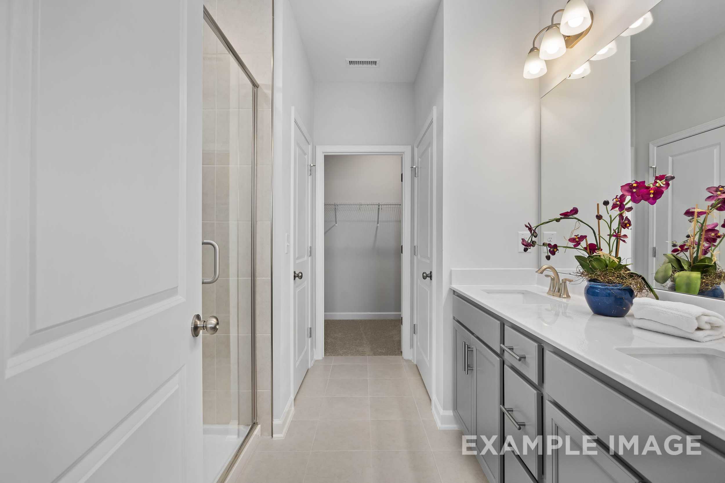Spacious master bathroom in The Daphne C featuring glass shower, gray vanity sink, and purple orchids