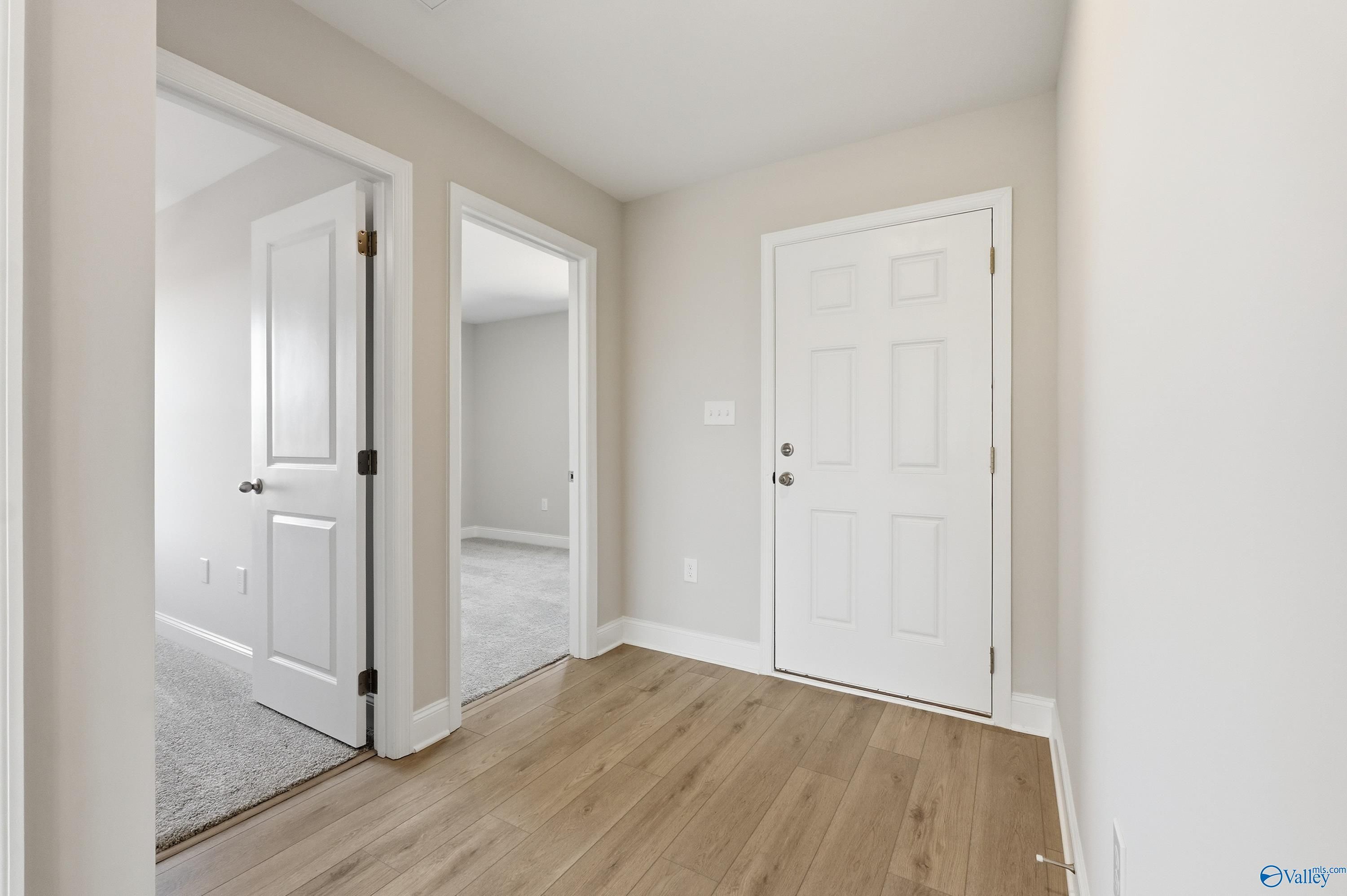 Bright hallway with white panel doors, beige walls, and oak hardwood floors in Davidson Homes The Butler 3-bedroom, New Market, Alabama