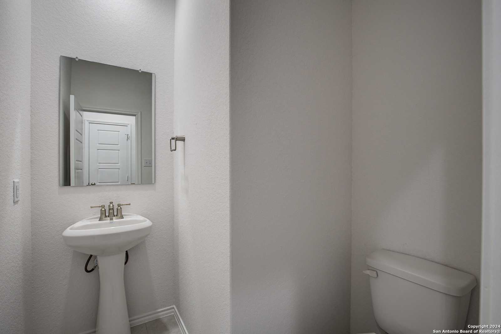 Bright half bath with white pedestal sink, mirror, and toilet in Davidson Homes The Douglas D, Seguin, Texas