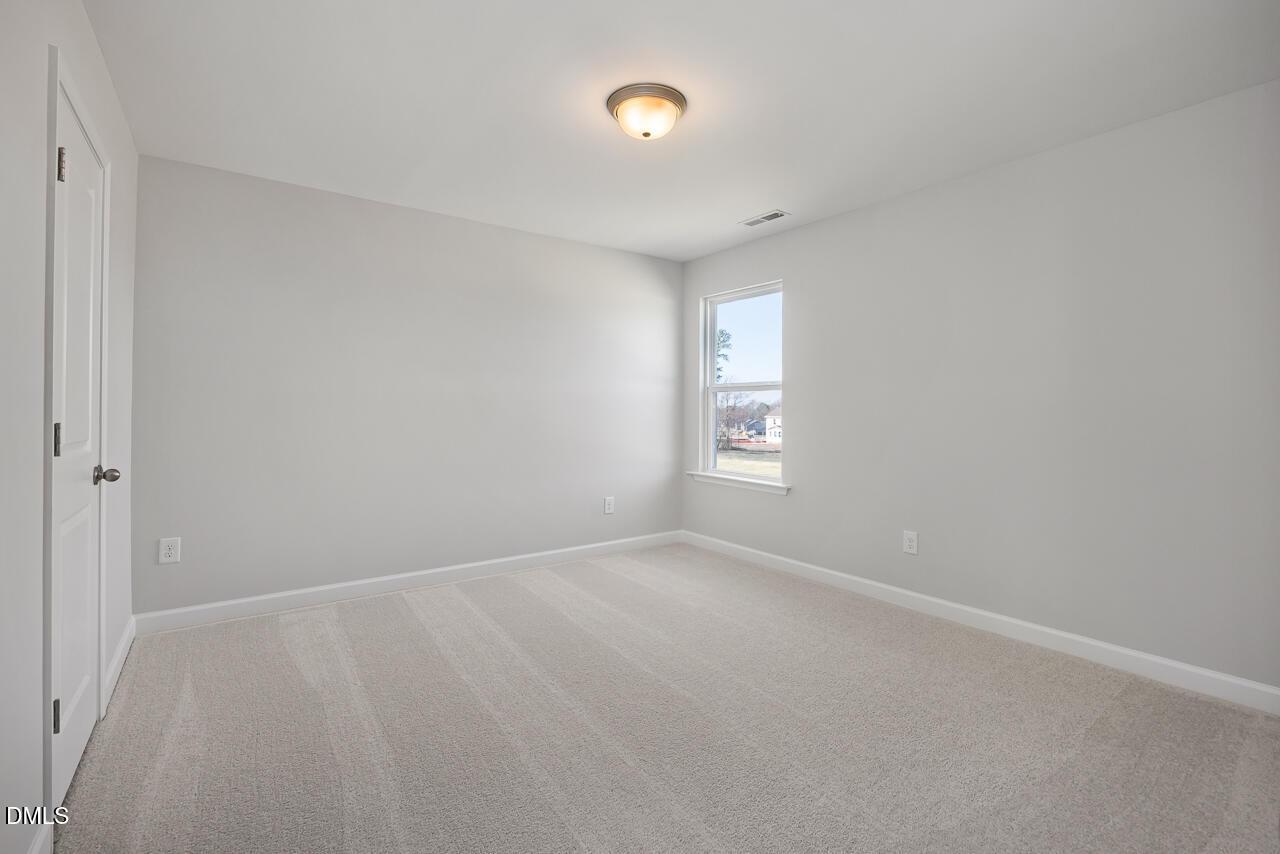 Empty bedroom featuring light gray walls, beige carpet, flush-mount ceiling light, and sunny window in Davidson Homes The Willow G, Angier, NC
