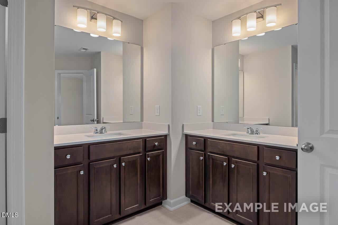 Elegant double vanity master bathroom with dark wood cabinets, white counters, and mirrors in Davidson Homes The Graham Interior, Fuquay-Varina, NC