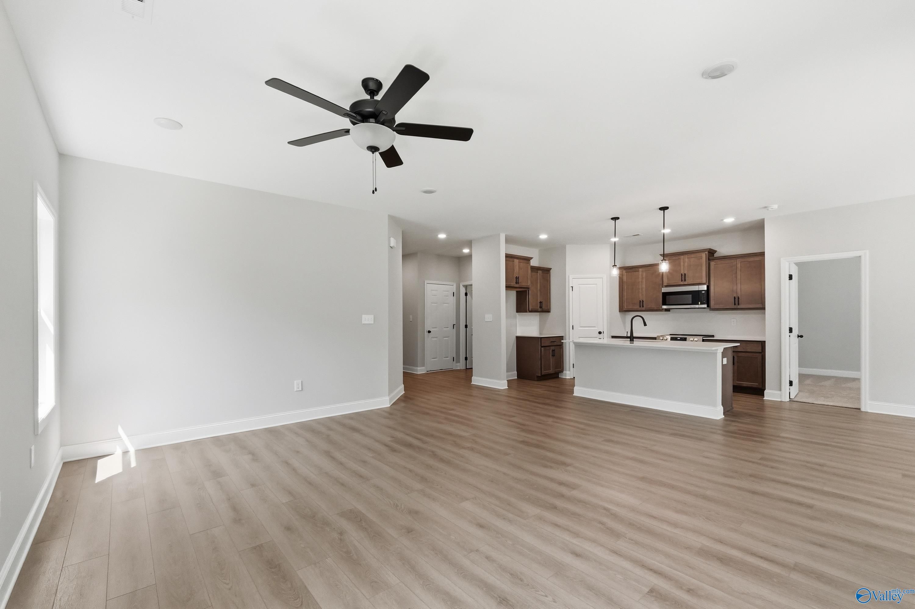 Open-concept living and kitchen with light hardwood floors, white island, shaker cabinets, ceiling fans in Davidson Homes The Franklin, Huntsville AL