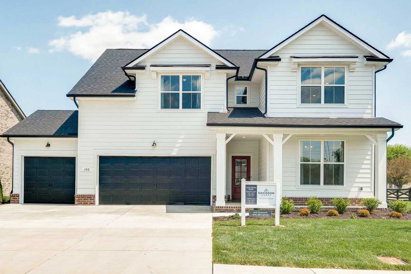 Classic white farmhouse home exterior at The Meadows in Smyrna TN with covered porch, red door and two-car garage