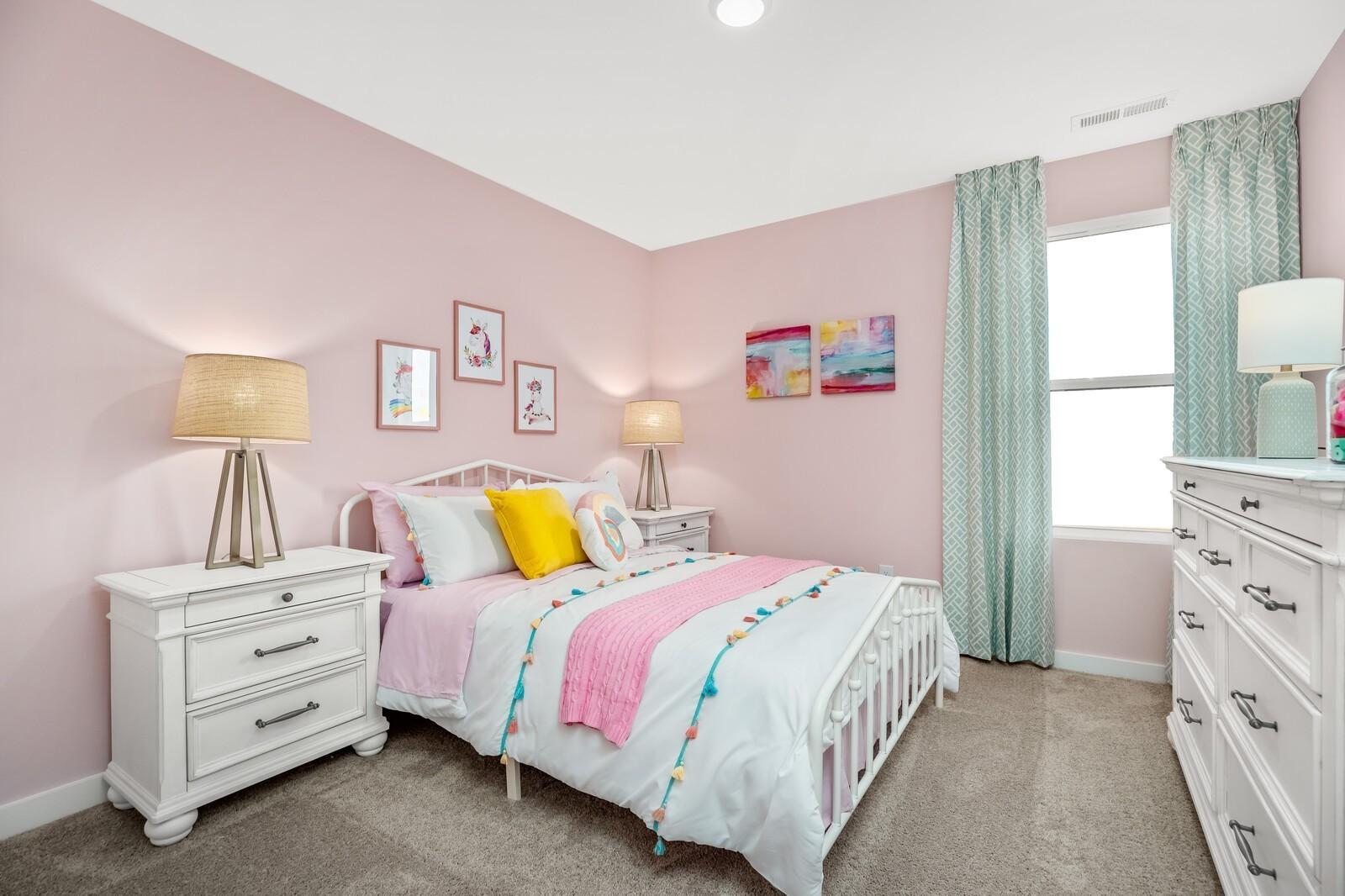 Charming pink girl's bedroom with white twin bed, colorful tassel bedding, lamps, and teal curtains in Davidson Homes The Gordon C, White House, Tennessee