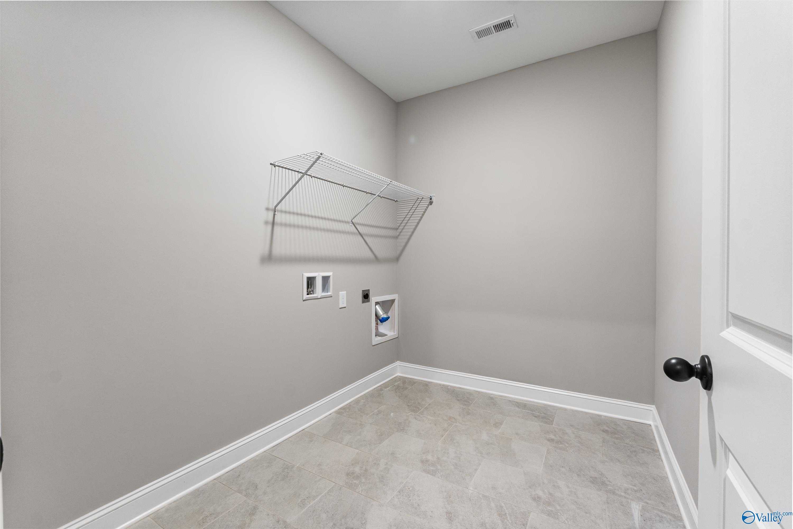 Modern laundry room with wire shelving, washer dryer hookups, and gray tile floor in The Finleigh home, Toney, Alabama