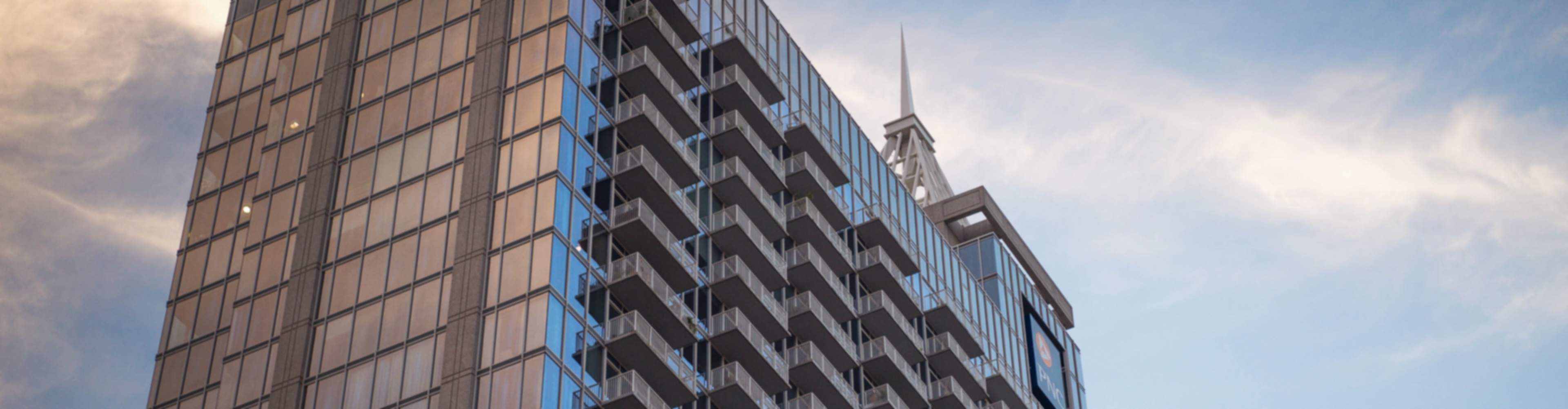Modern high-rise apartment building with reflective glass facade, balconies, and spire in Raleigh