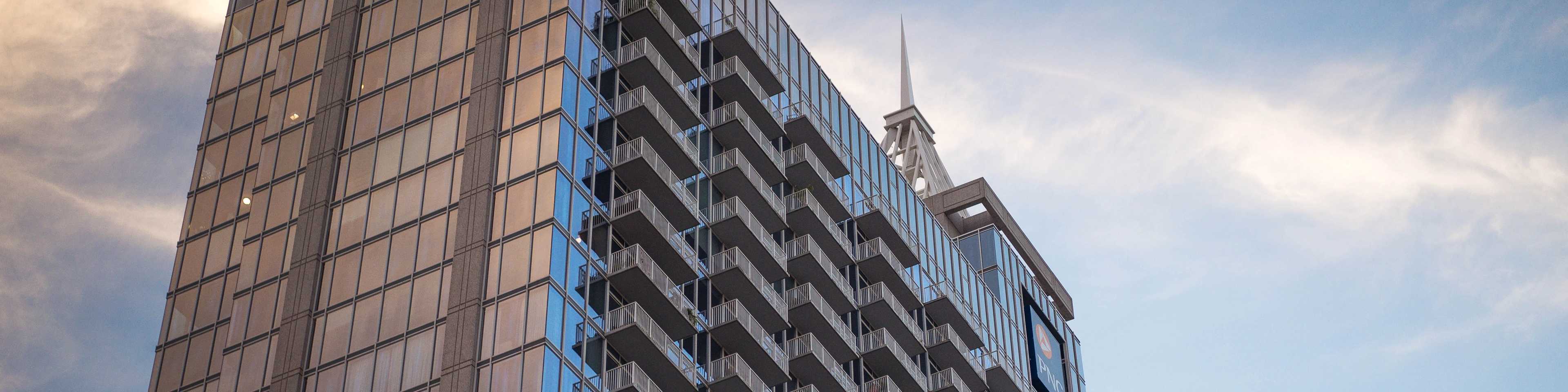 Modern high-rise apartment building with reflective glass facade, balconies, and spire in Raleigh