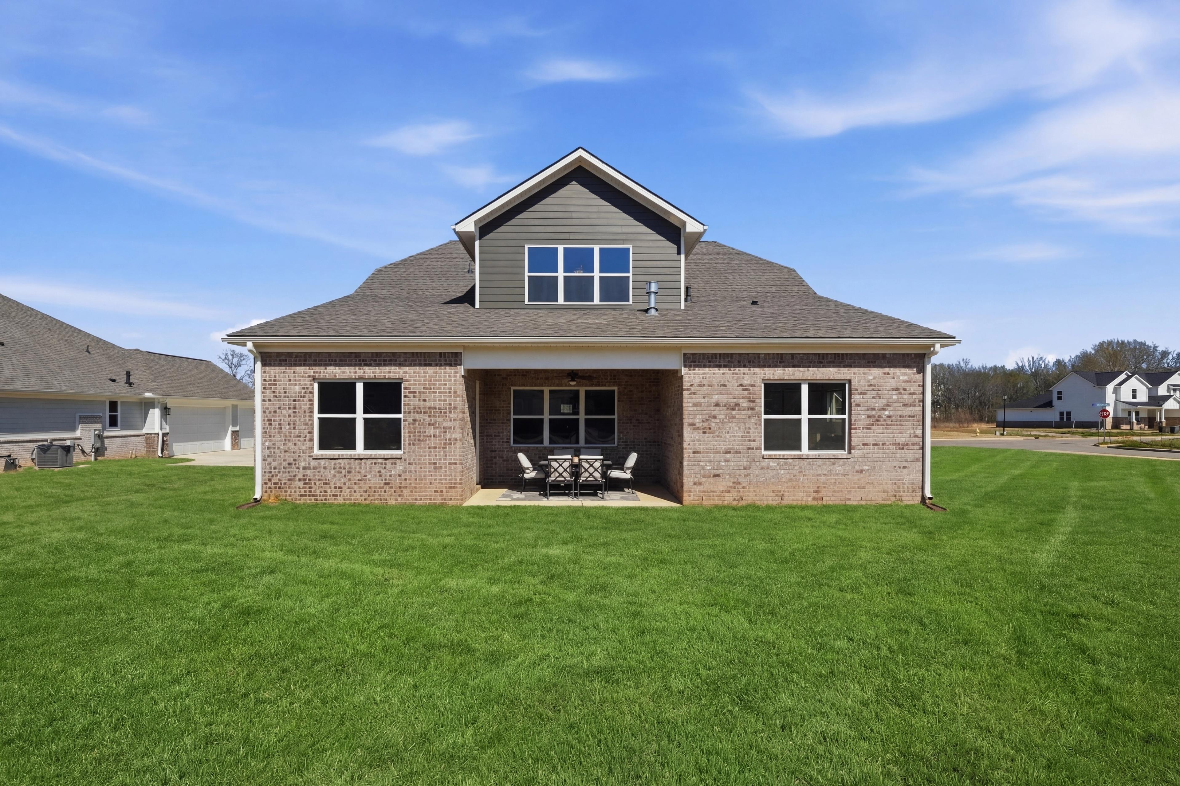 Brick home exterior with covered porch, patio seating, and lush green lawn at The Meadows at Hampton Cove, Owens Cross Roads AL