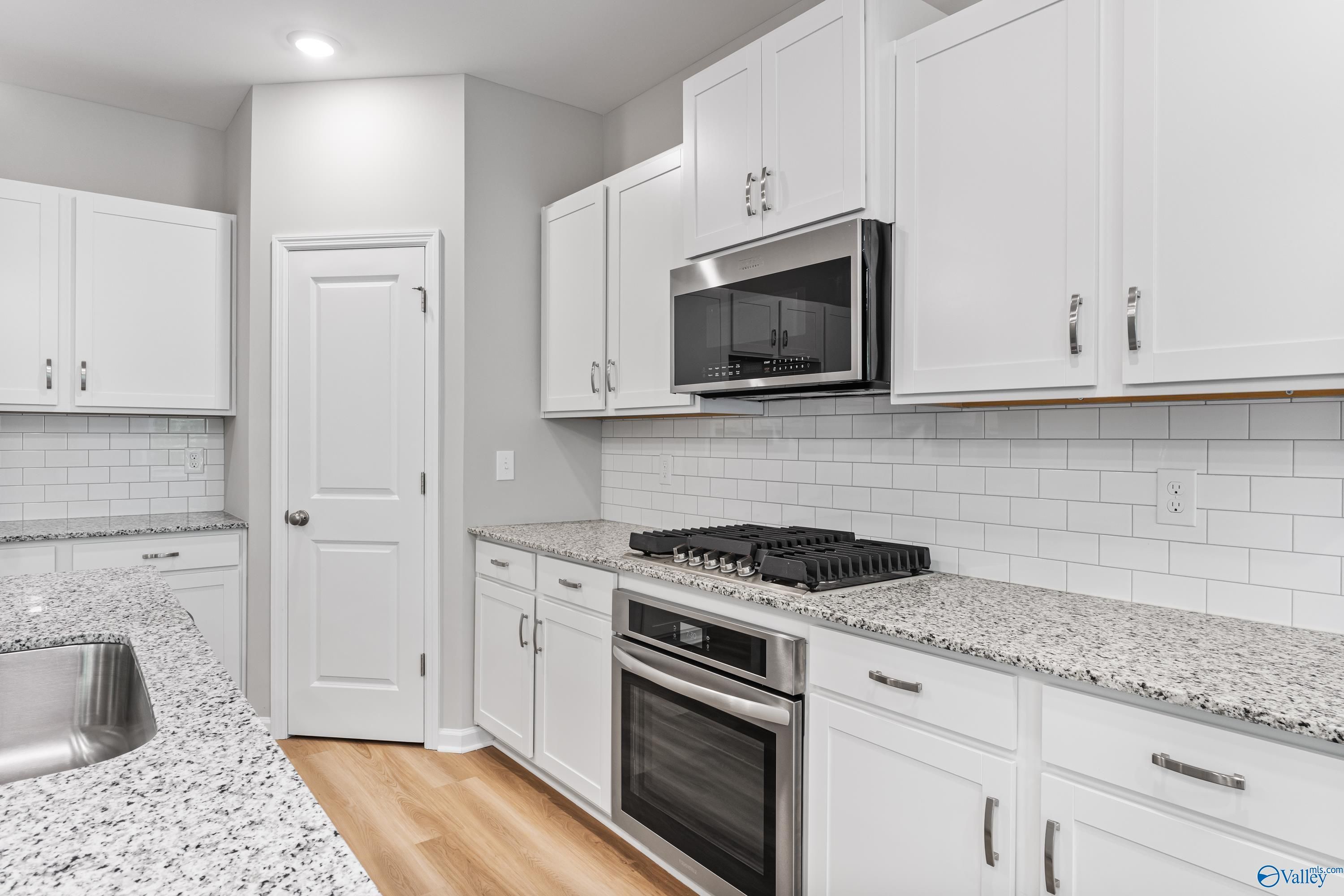 Modern kitchen featuring white shaker cabinets, speckled granite counters, stainless appliances, subway tile backsplash in Davidson Homes The Phoenix, Hazel Green, Alabama