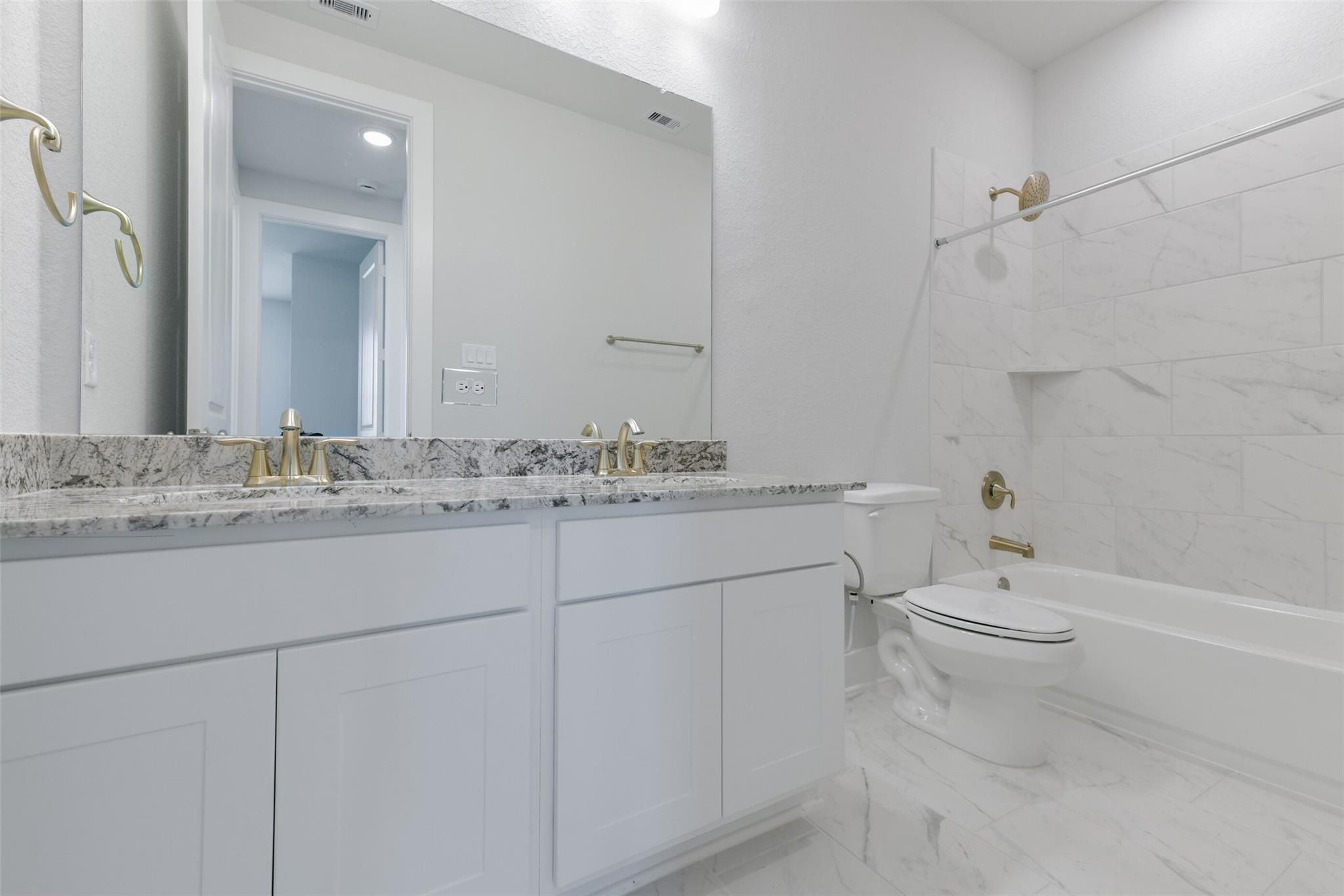 Elegant double vanity bathroom with white cabinets, gold fixtures, and marble tiles in Davidson Homes The Edward A, Lago Mar, Texas City