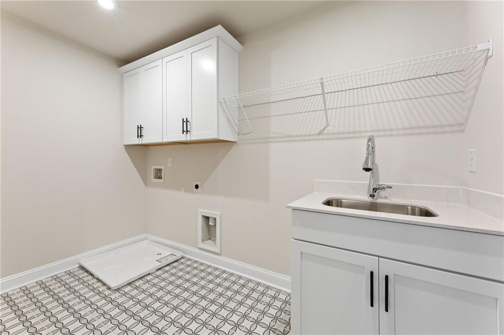 Modern laundry room with white cabinets, utility sink, wire shelving, and patterned tile floor in The Hickory E by Davidson Homes, Buford, Georgia