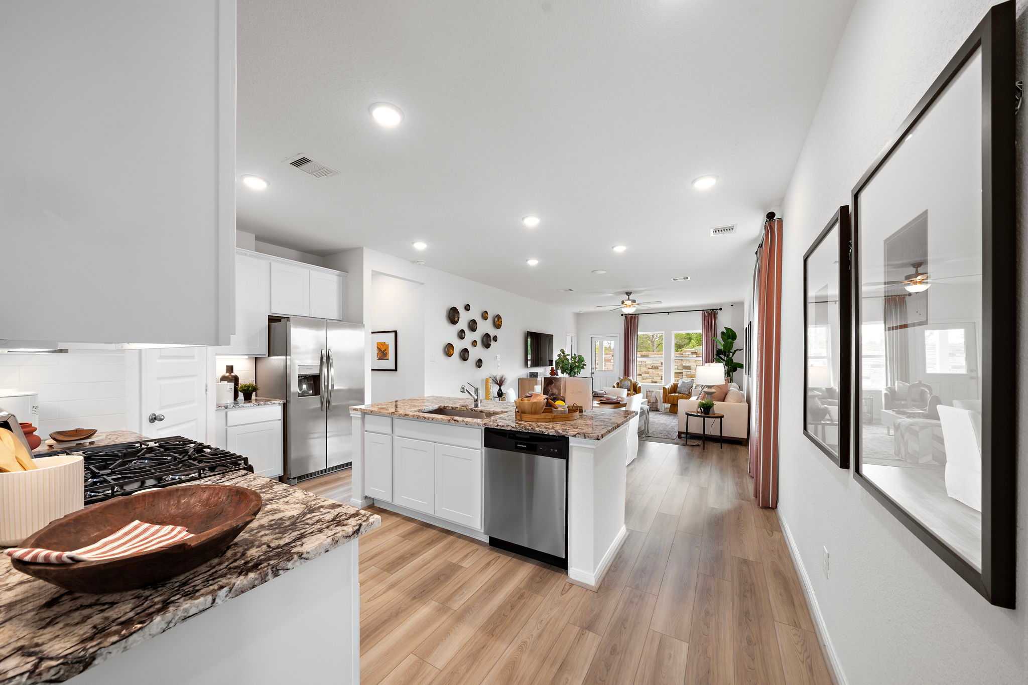 Open-concept kitchen and living room at The Villages at WestPointe in Dayton Texas with white cabinets, granite island, hardwood floors and large windows
