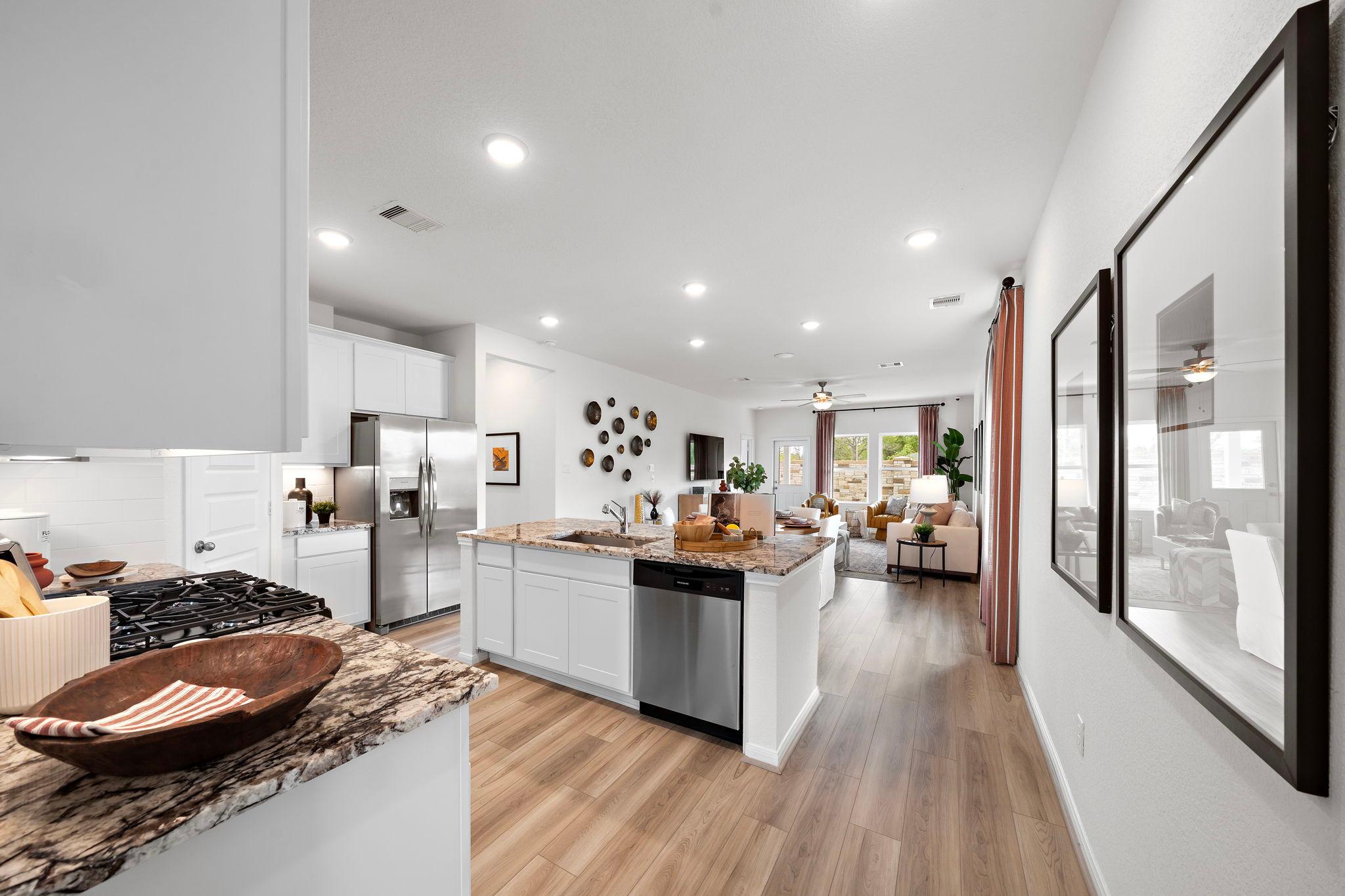 Open-concept kitchen and living room at The Villages at WestPointe in Dayton Texas with white cabinets, granite island, hardwood floors and large windows